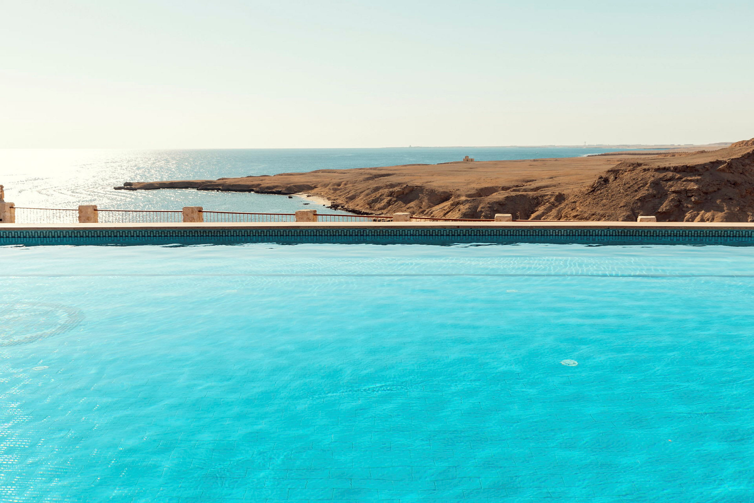 Bild av en pool med klarblått vatten och utsikt över havet och torr landskap. (AI-genererad text)