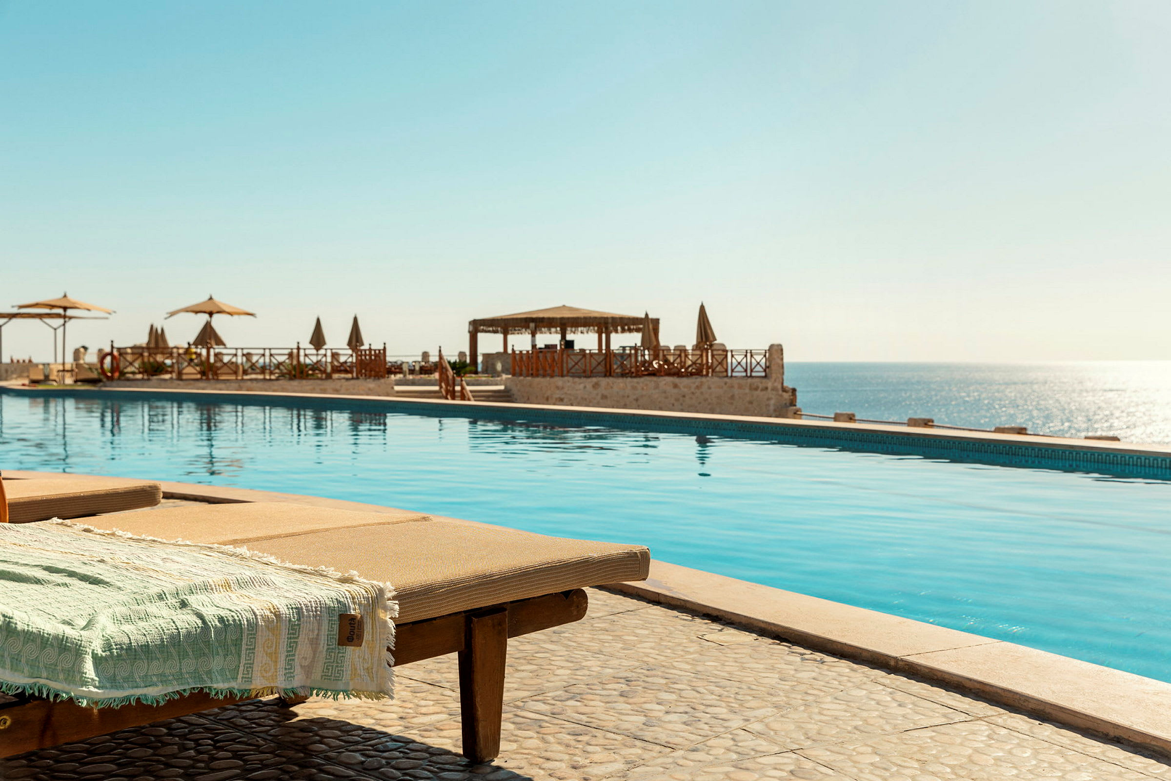 Solstolar vid en swimmingpool med havet i bakgrunden. (AI-genererad text)