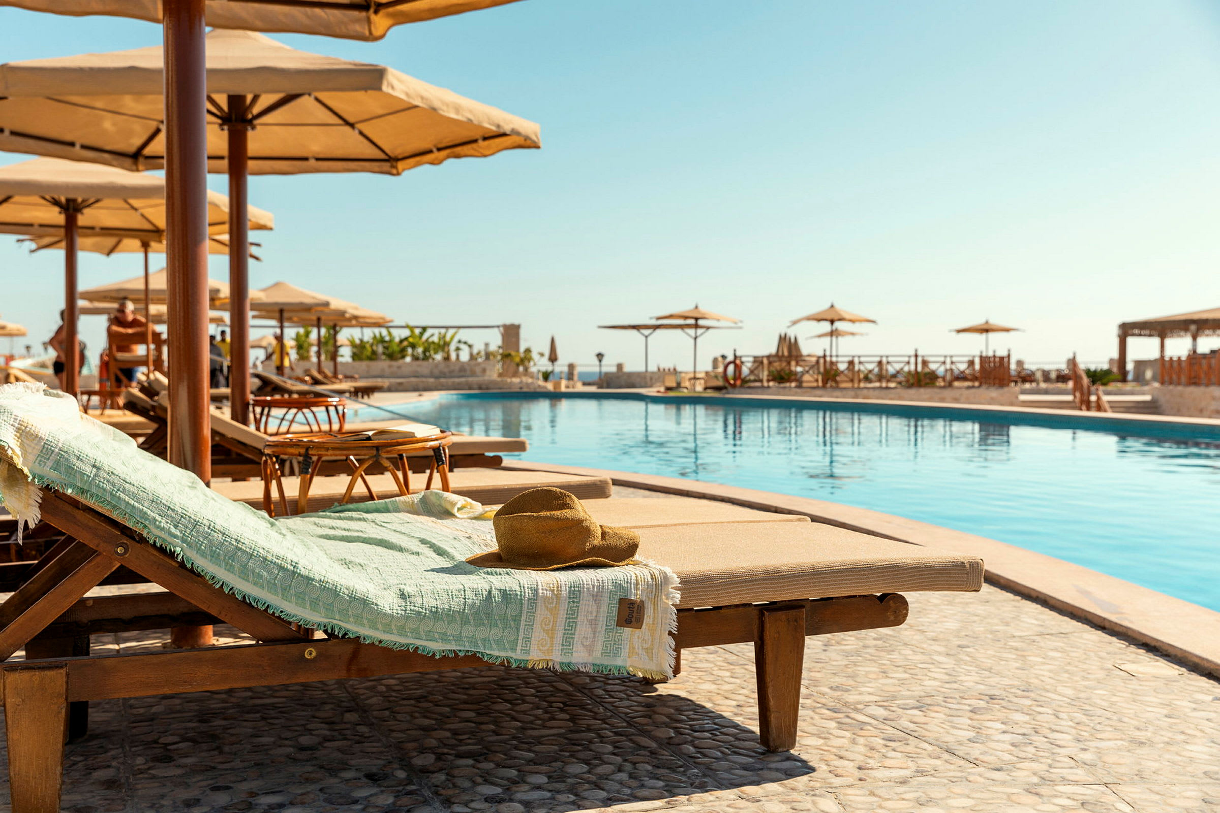 Solstol vid en pool med parasoller i bakgrunden. (AI-genererad text)