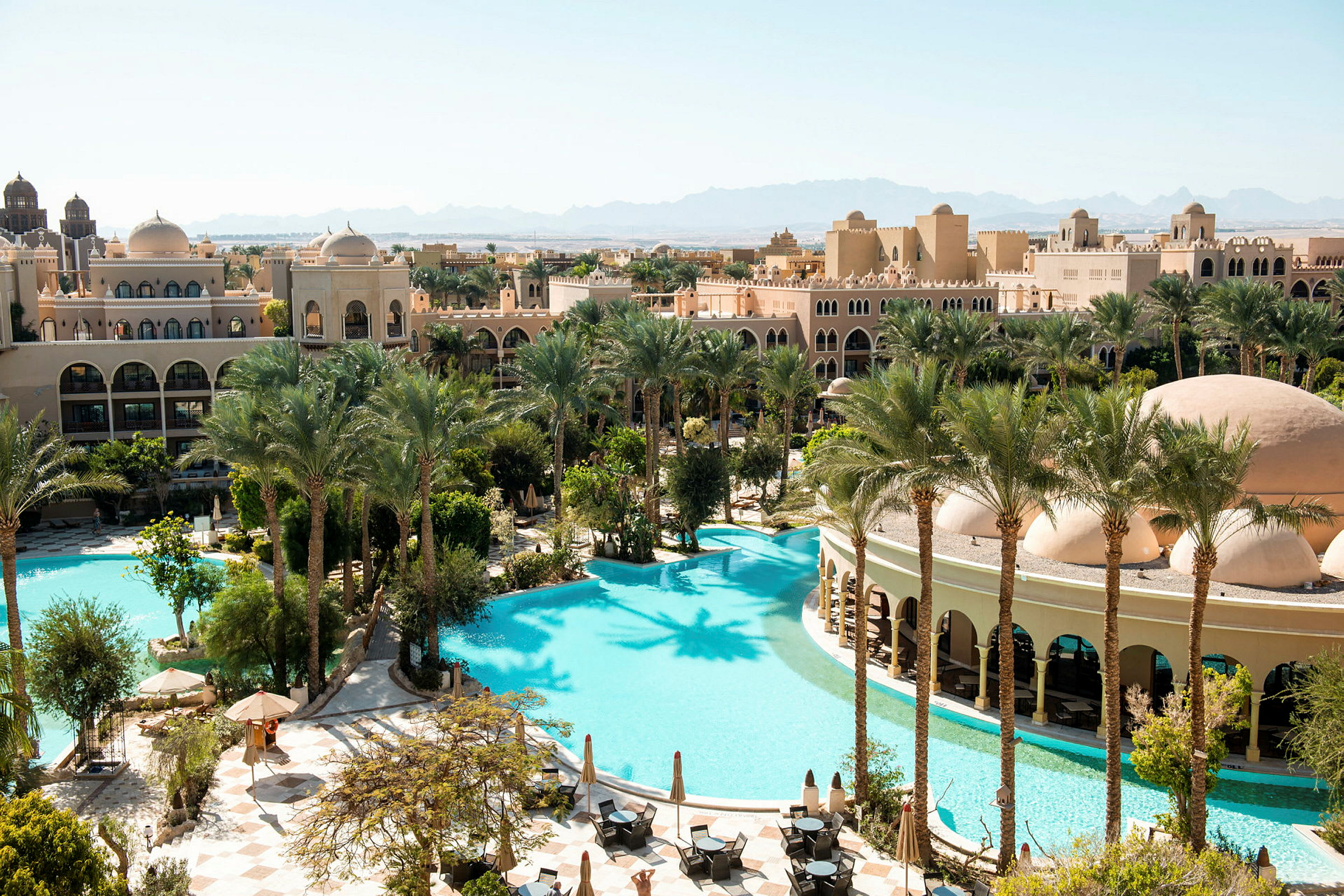 Ett hotellområde med pooler, palmer och byggnader i arabisk arkitektur. (AI-genererad text)