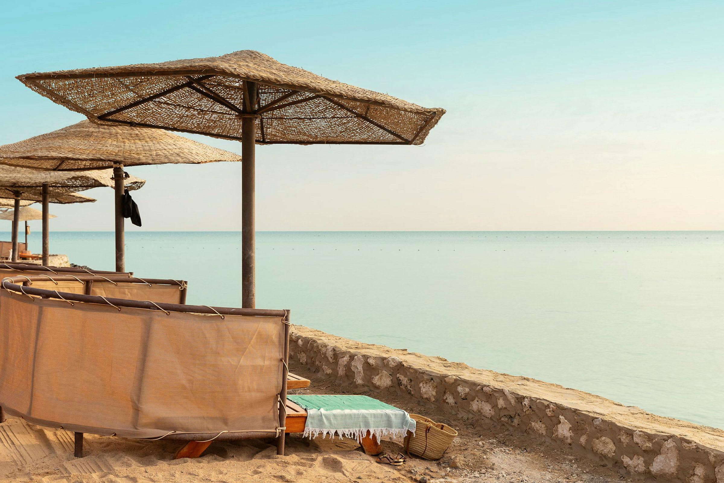 Strand med solstolar under halmtak och utsikt över stilla hav. (AI-genererad text)