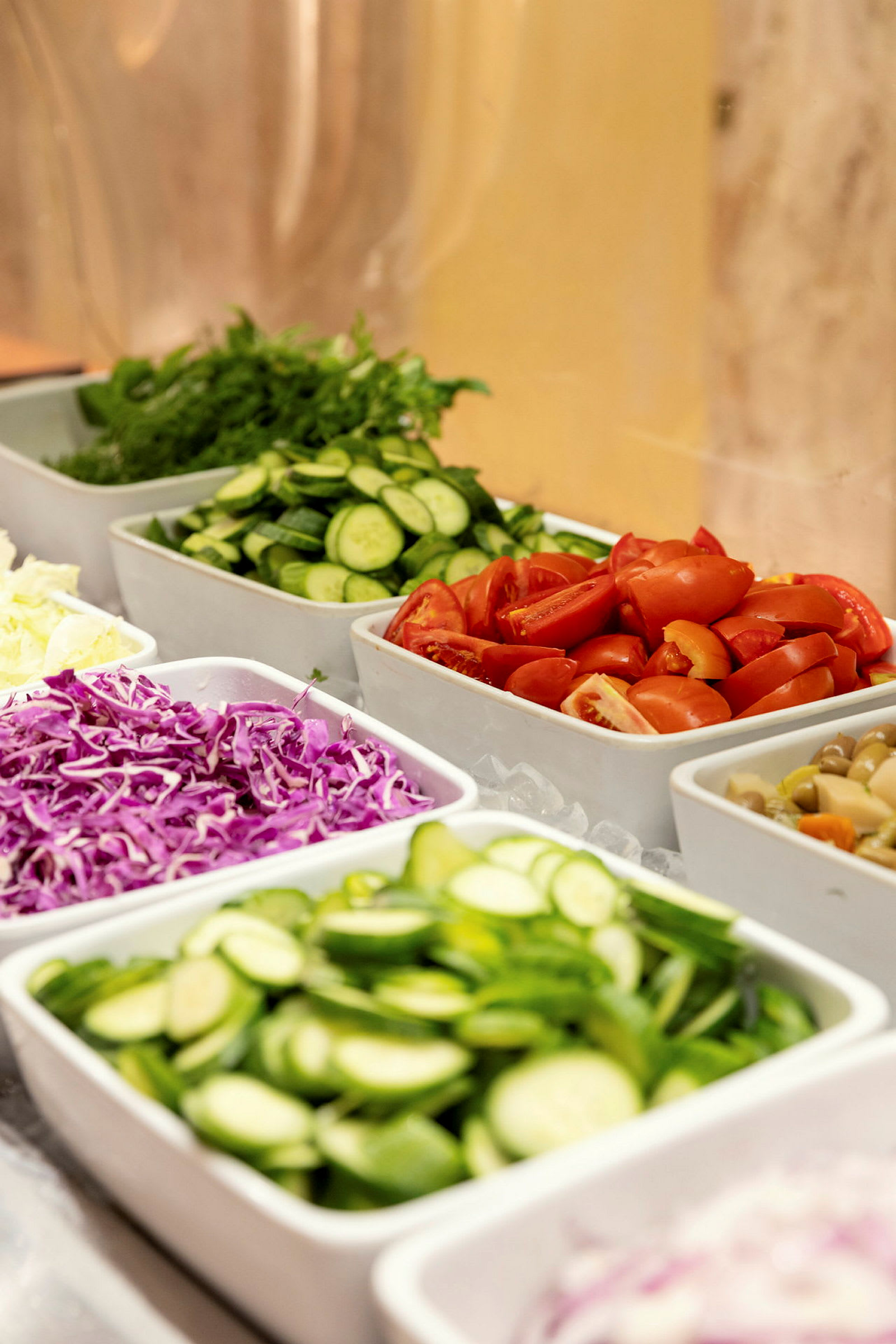 En buffé med olika grönsaker som tomater, gurka, rödkål och sallad upplagda i vita skålar. (AI-genererad text)