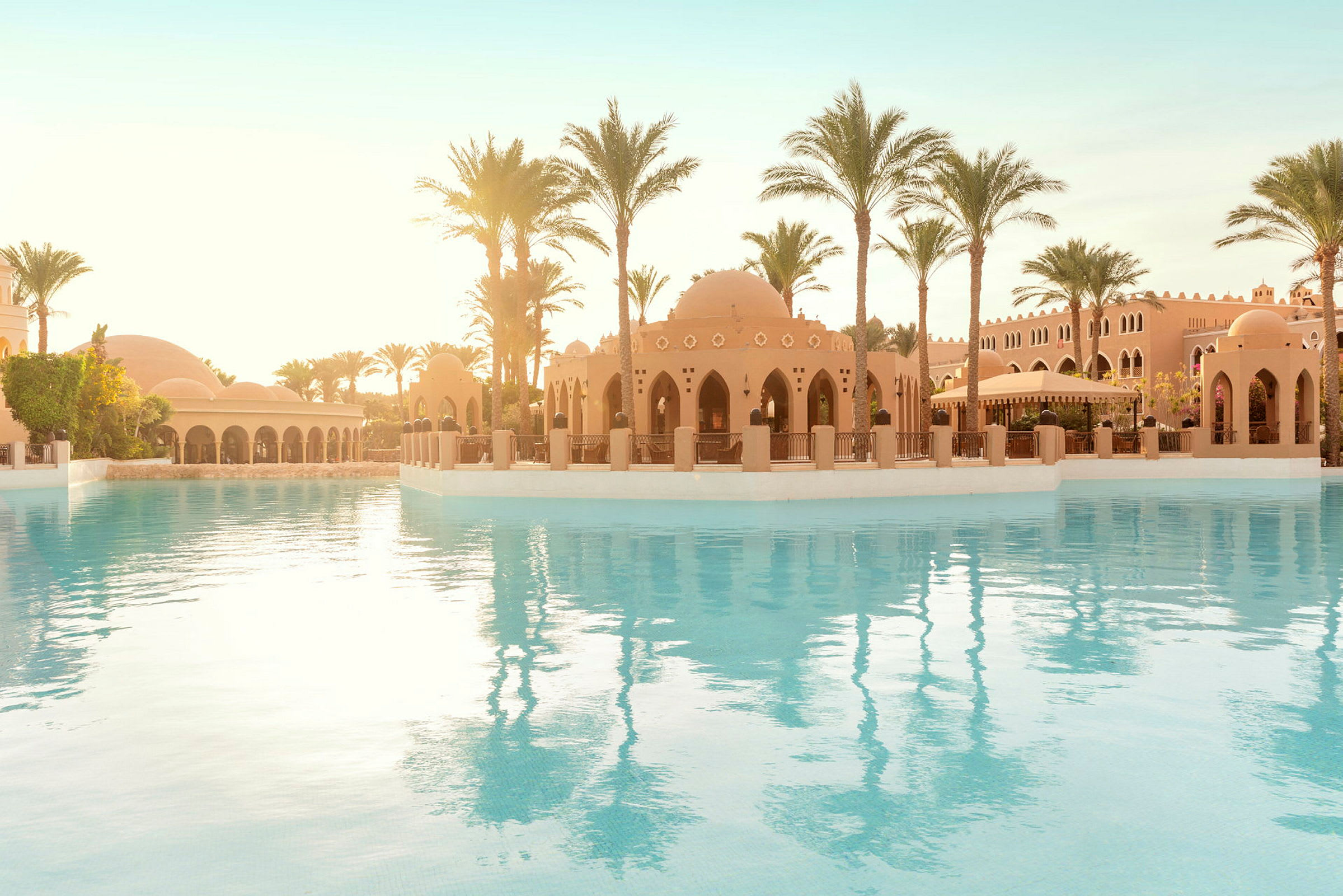 Bild av en elegant pool framför en byggnad i orientalisk stil omgiven av palmer. (AI-genererad text)