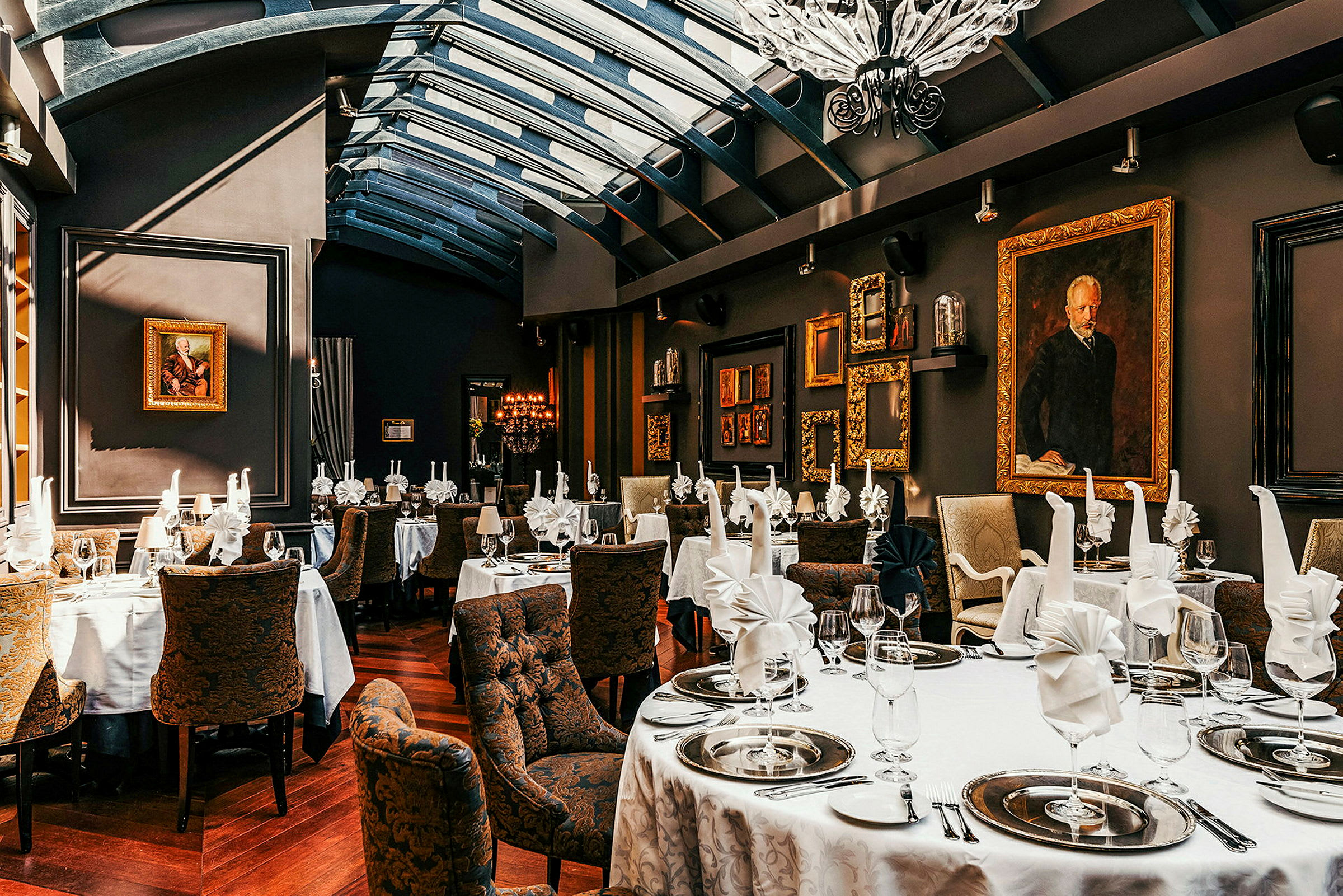 Bilden visar en elegant restaurang med dukade bord, vita dukar, vikta servetter och dekorativa tallrikar. Väggarna är dekorerade med konstverk och guldramar. (AI-genererad text)