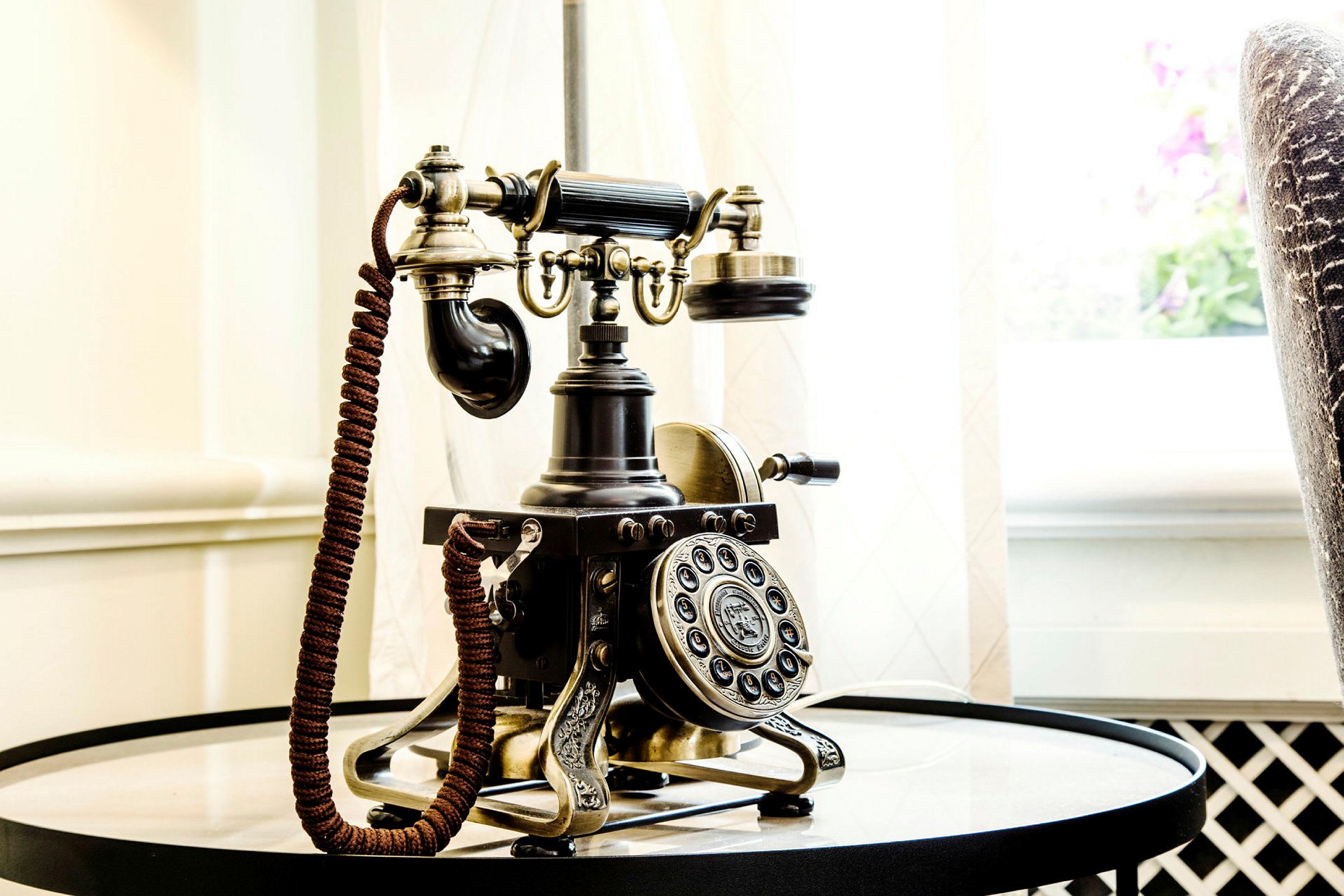 Antik telefon på ett runt bord nära ett ljusinsläpp. (AI-genererad text)