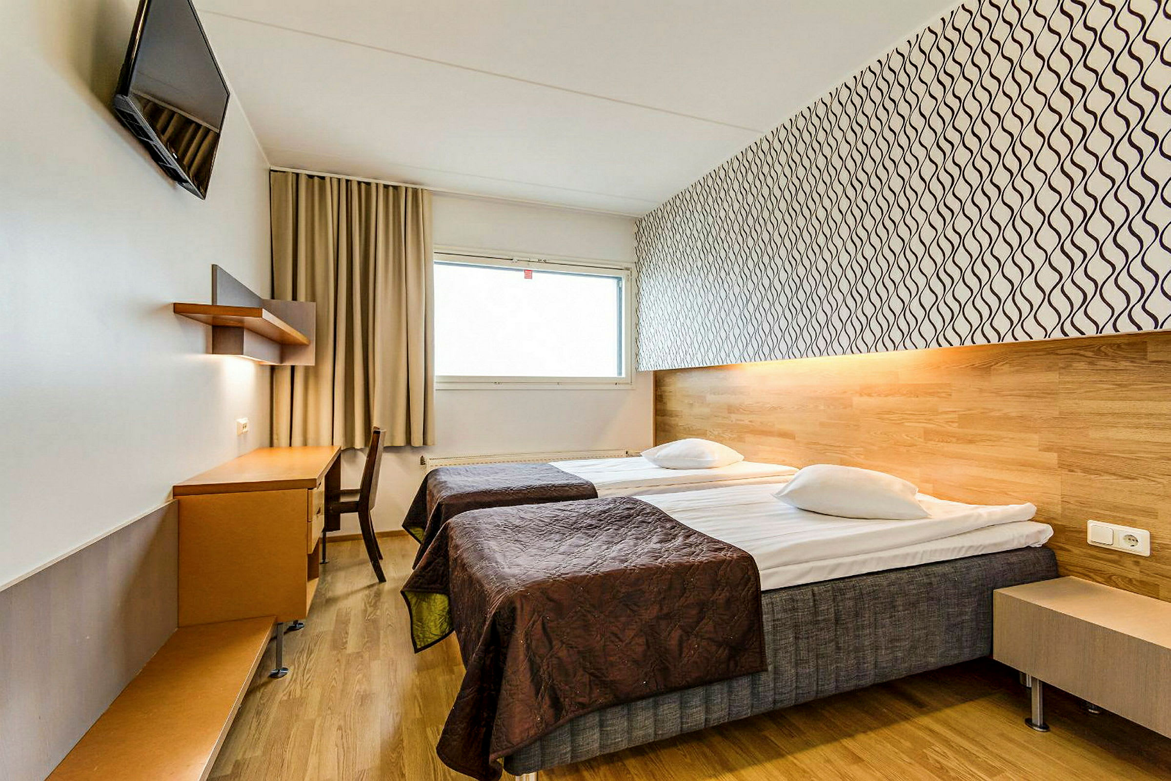 Ett hotellrum med två enkelsängar, ett skrivbord och en väggmonterad TV. (AI-genererad text)