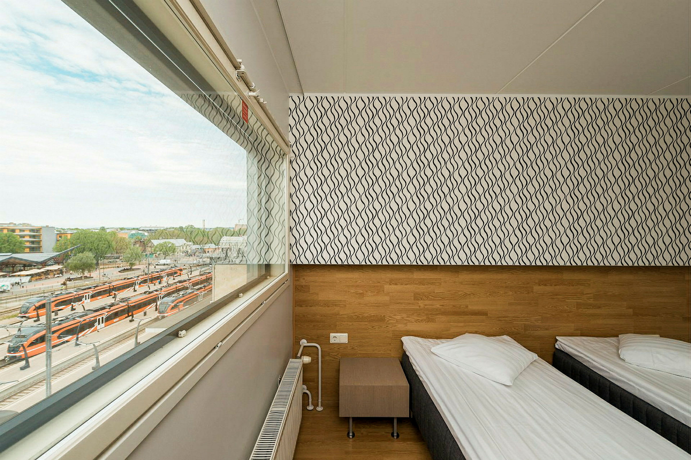Ett enkelt hotellrum med två enkelsängar, ett fönster med utsikt över en tågstation. (AI-genererad text)