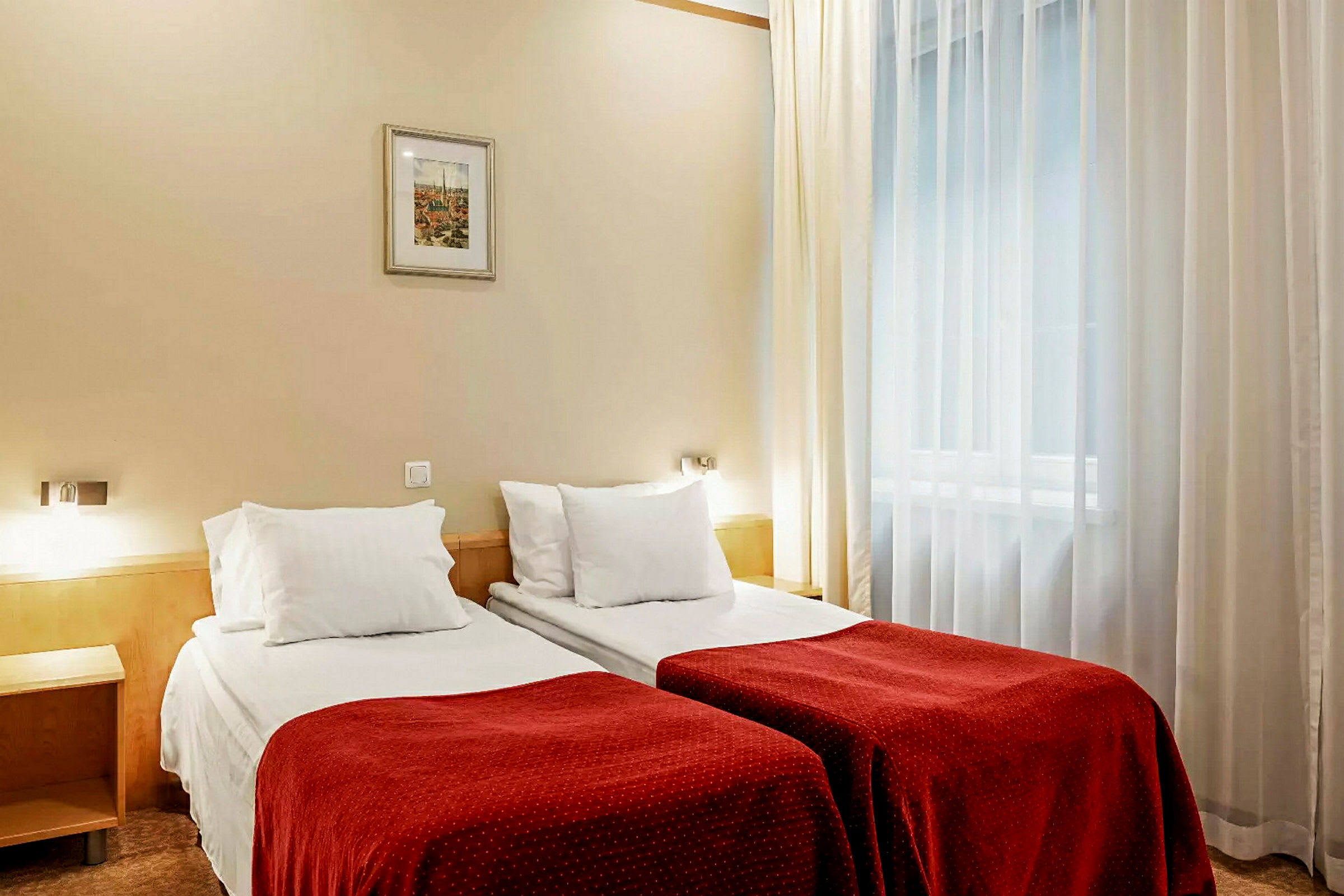 Två enkelsängar med röda överkast och vita kuddar i ett hotellrum. (AI-genererad text)