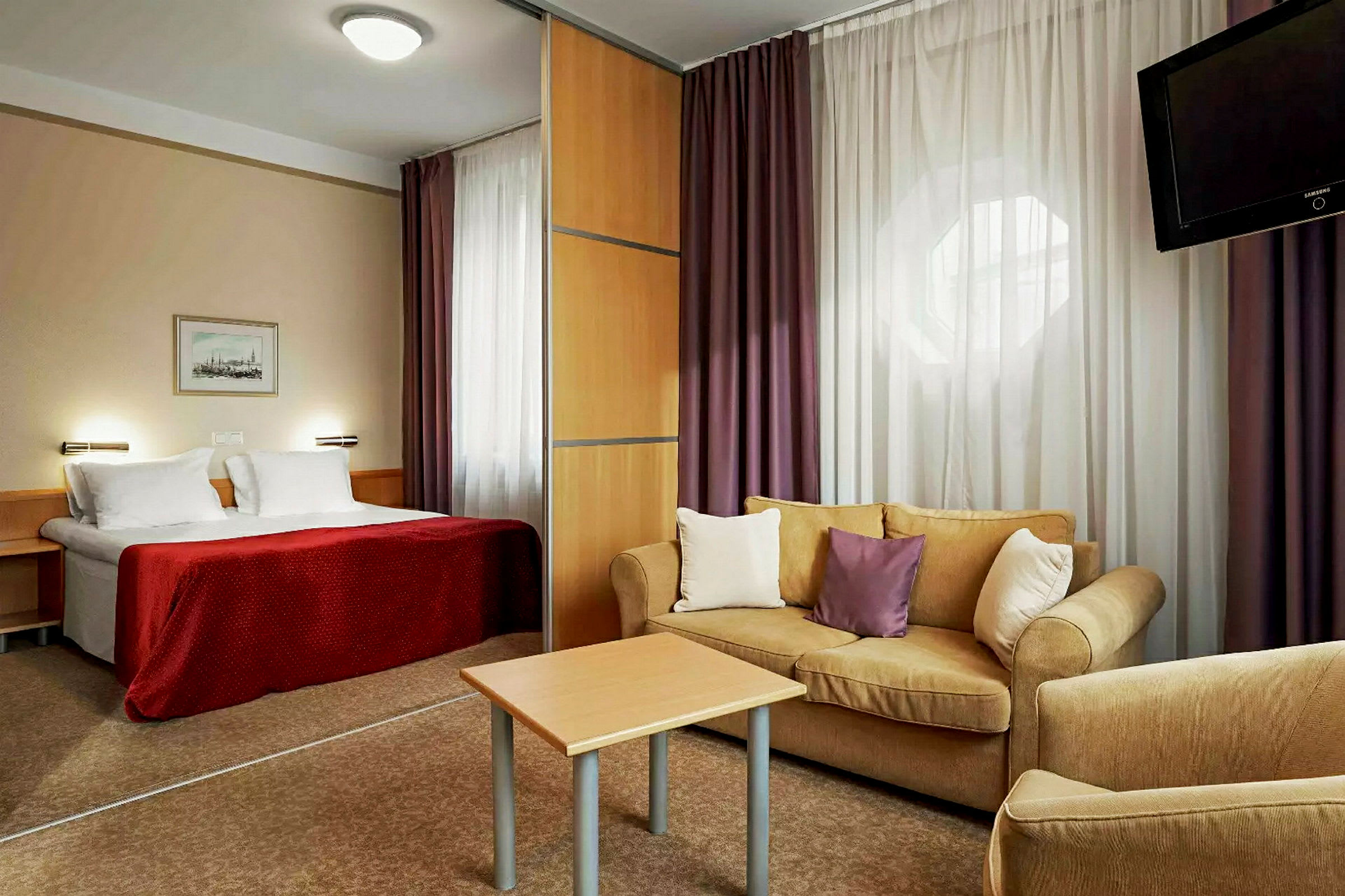 Hotellrum med en säng, ett vardagsrum med soffa och ett bord samt en TV. (AI-genererad text)