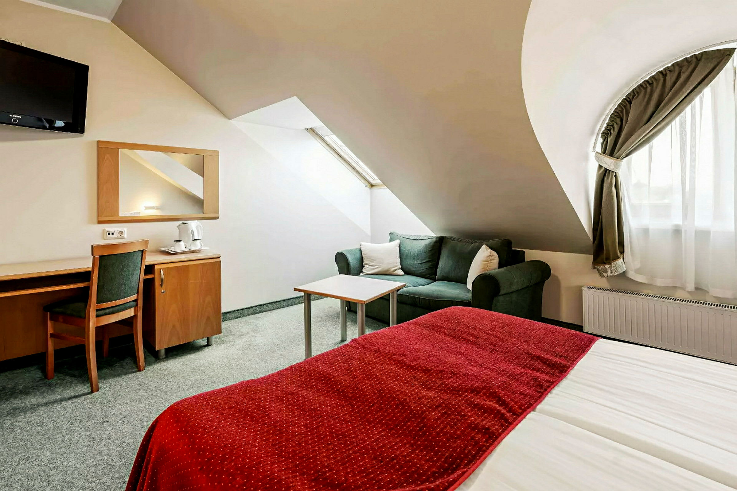 Ett hotellrum med en säng med rött täcke, en soffa och ett skrivbord med stol. (AI-genererad text)