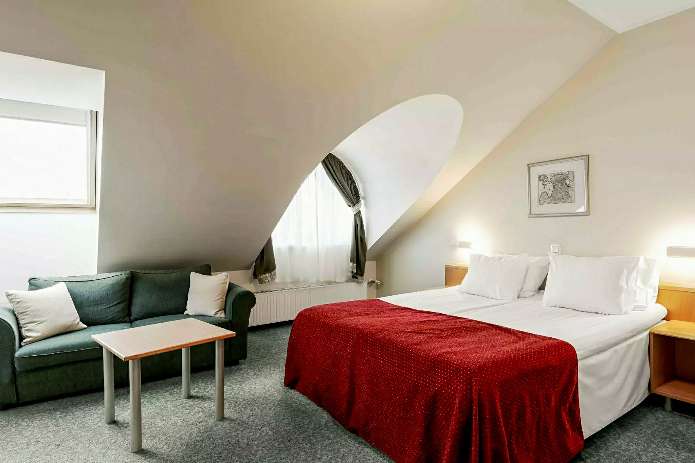 Ett hotellrum med en dubbelsäng, en grön soffa och ett litet bord. (AI-genererad text)