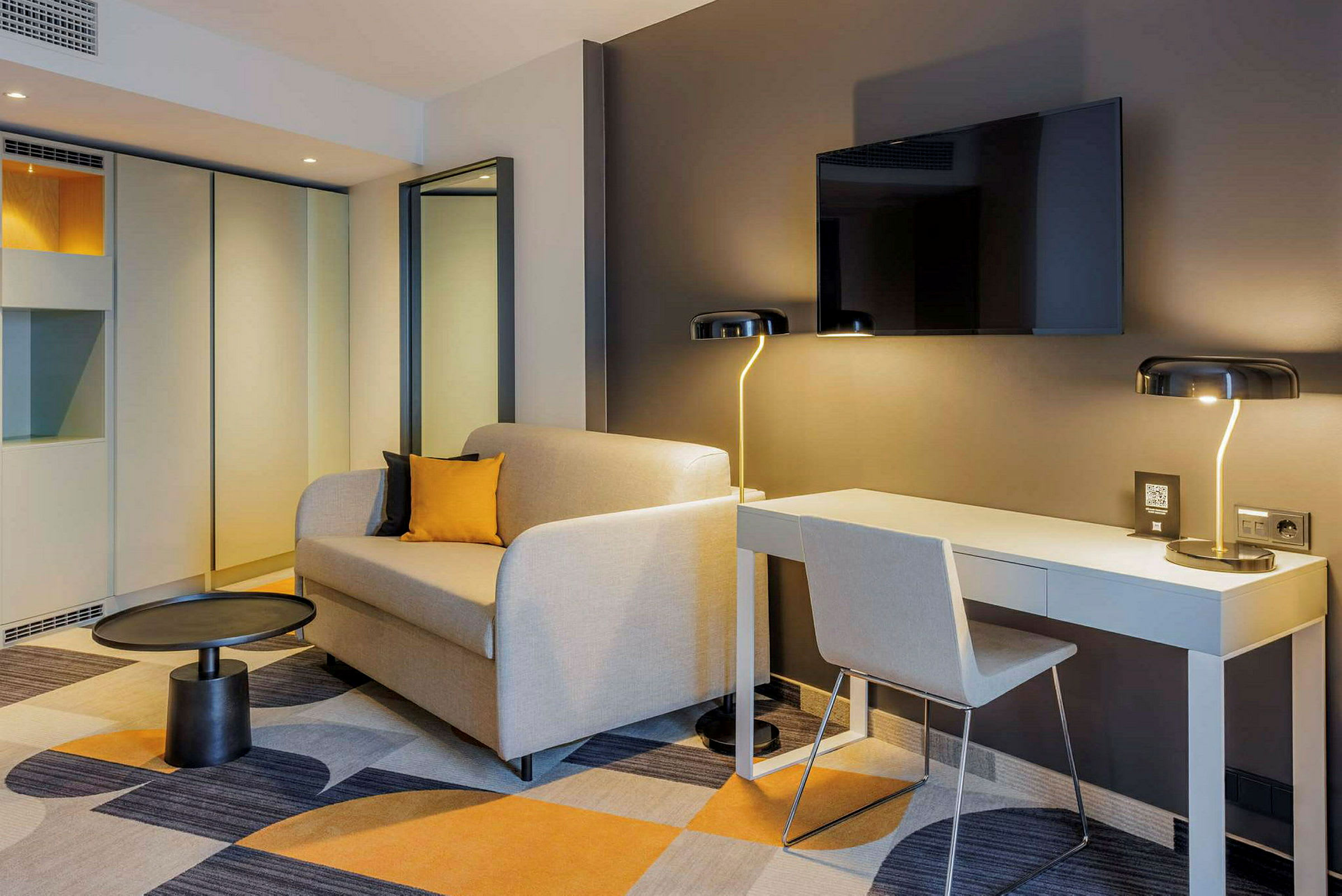 Ett modernt hotellrum med en soffa, ett skrivbord och en väggmonterad TV. (AI-genererad text)