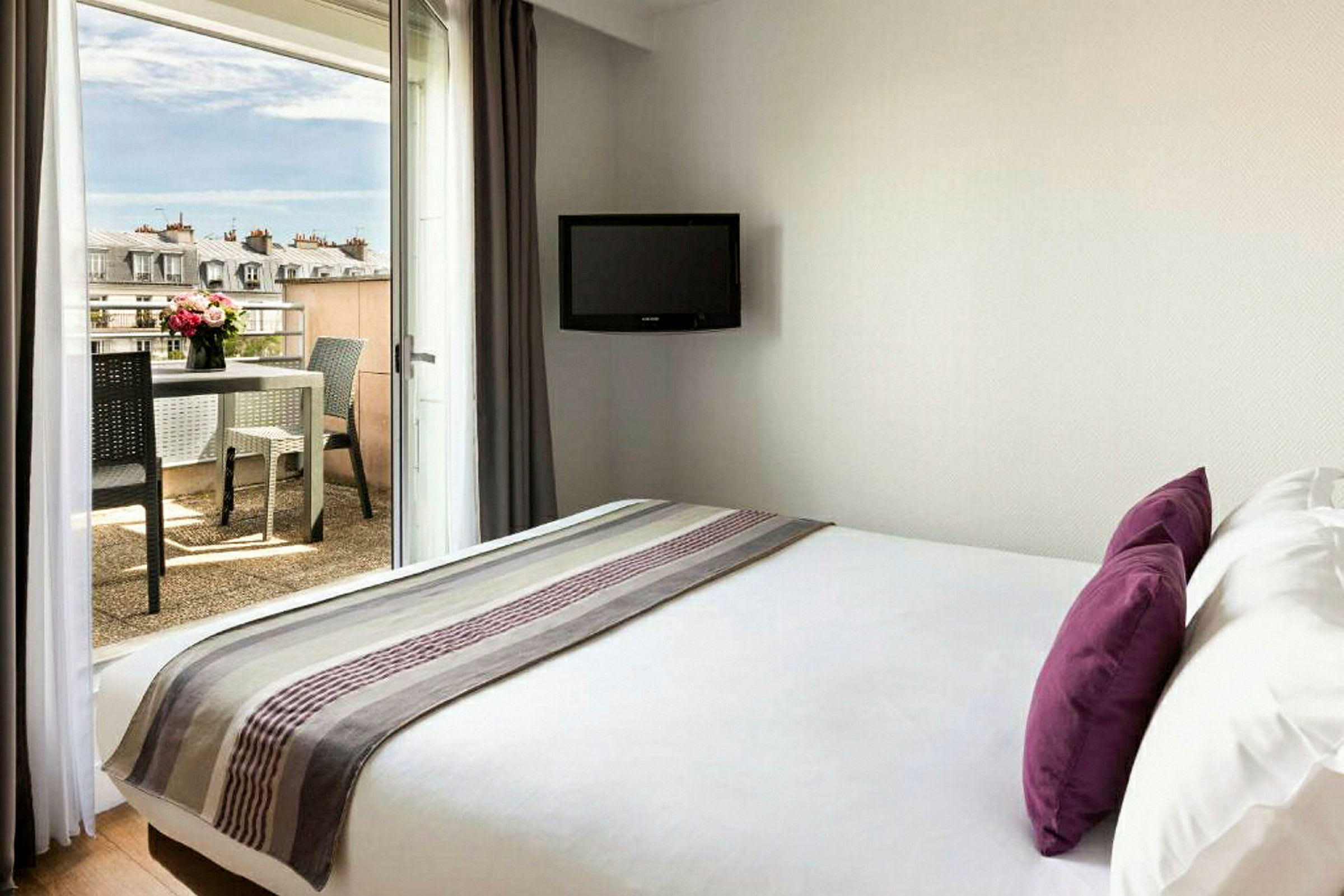 Hotellrum med säng, TV på väggen och balkong med bord och stolar. (AI-genererad text)