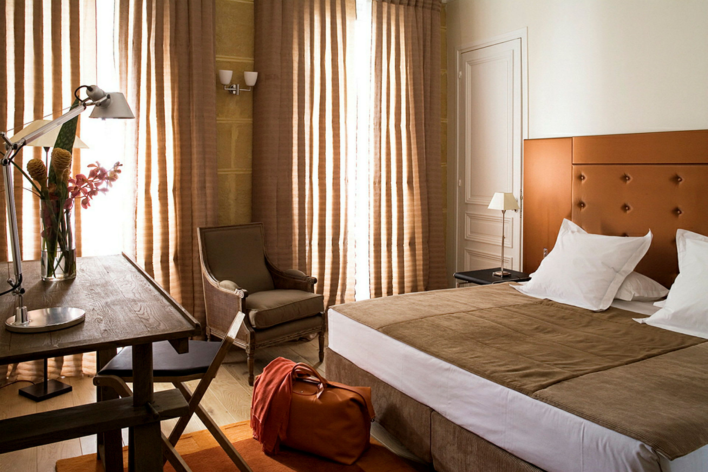 Ett hotellrum med en säng, stol, bord och gardiner. (AI-genererad text)