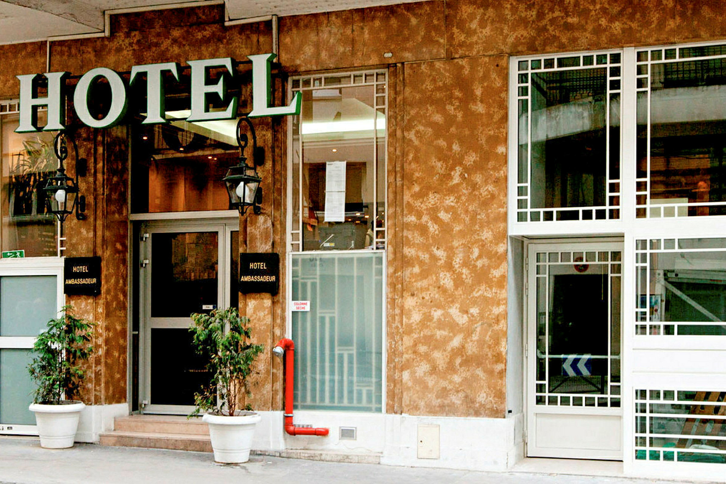 Framsidan av ett hotell med en skylt som säger 'Hotel Ambassadeur'. (AI-genererad text)