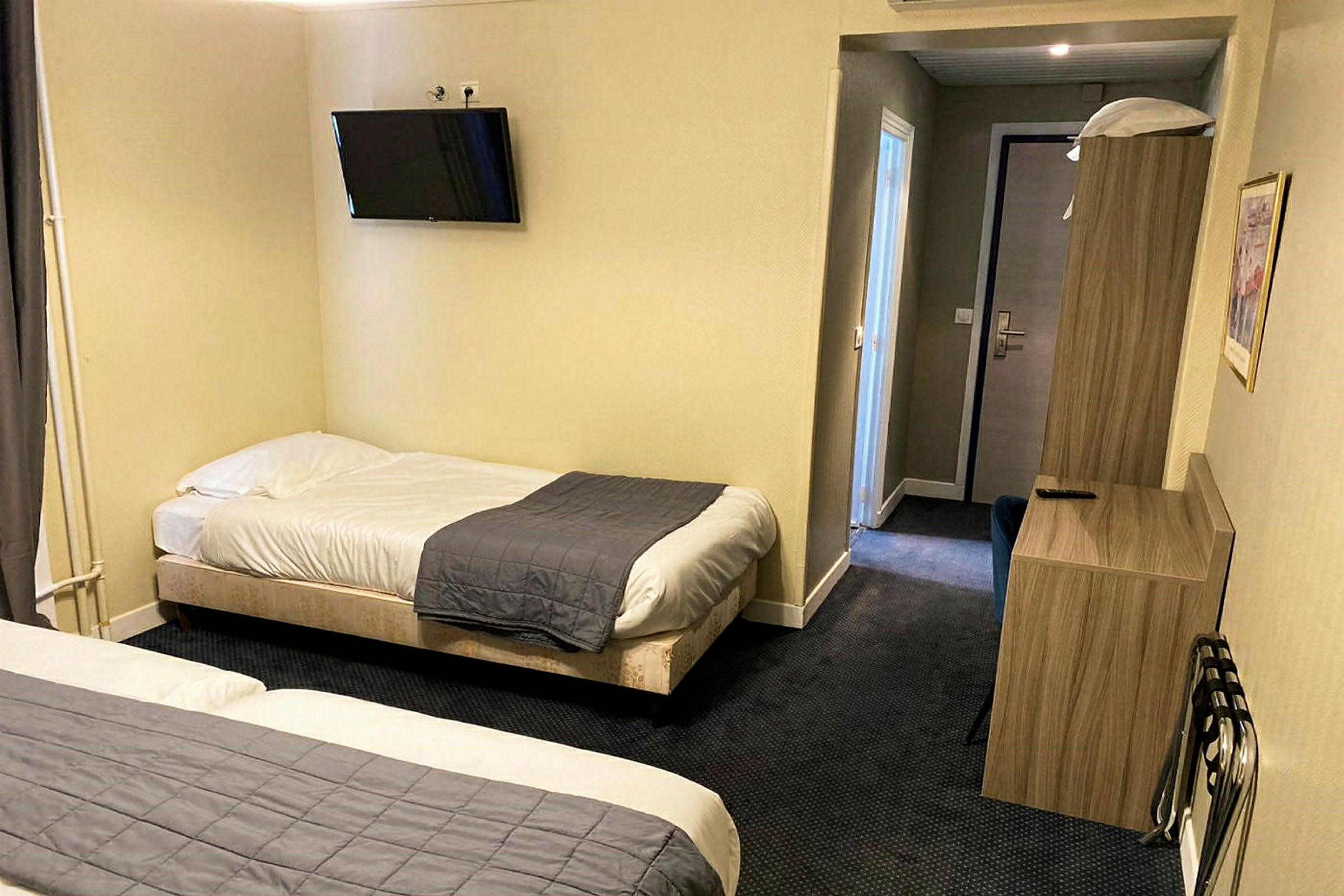Ett hotellrum med två enkelsängar, en väggmonterad TV och möbler. (AI-genererad text)