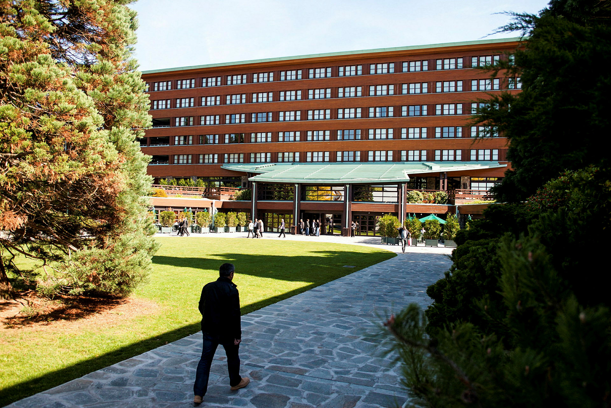 En byggnad med en modern entré omgiven av grönska och gångvägar. (AI-genererad text)