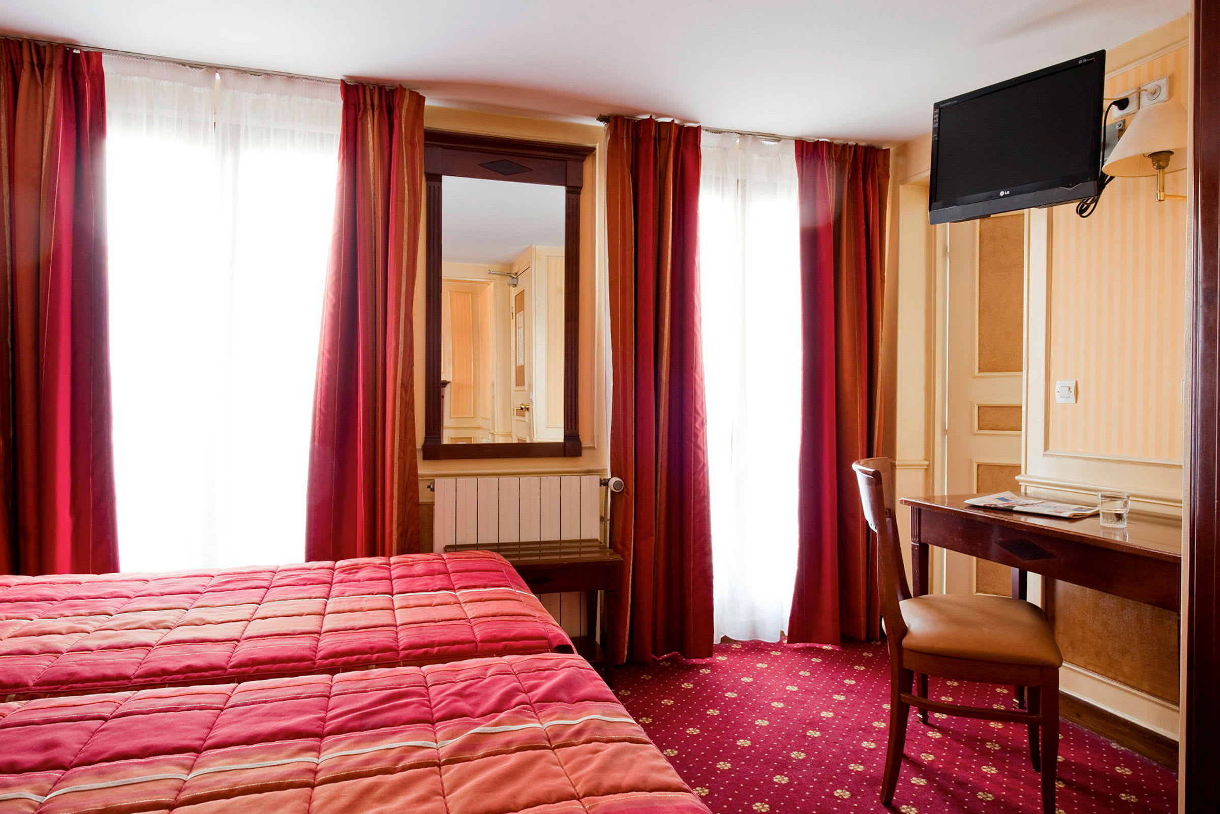Ett hotellrum med två sängar, en spegel, en väggmonterad TV och ett skrivbord med stol. (AI-genererad text)