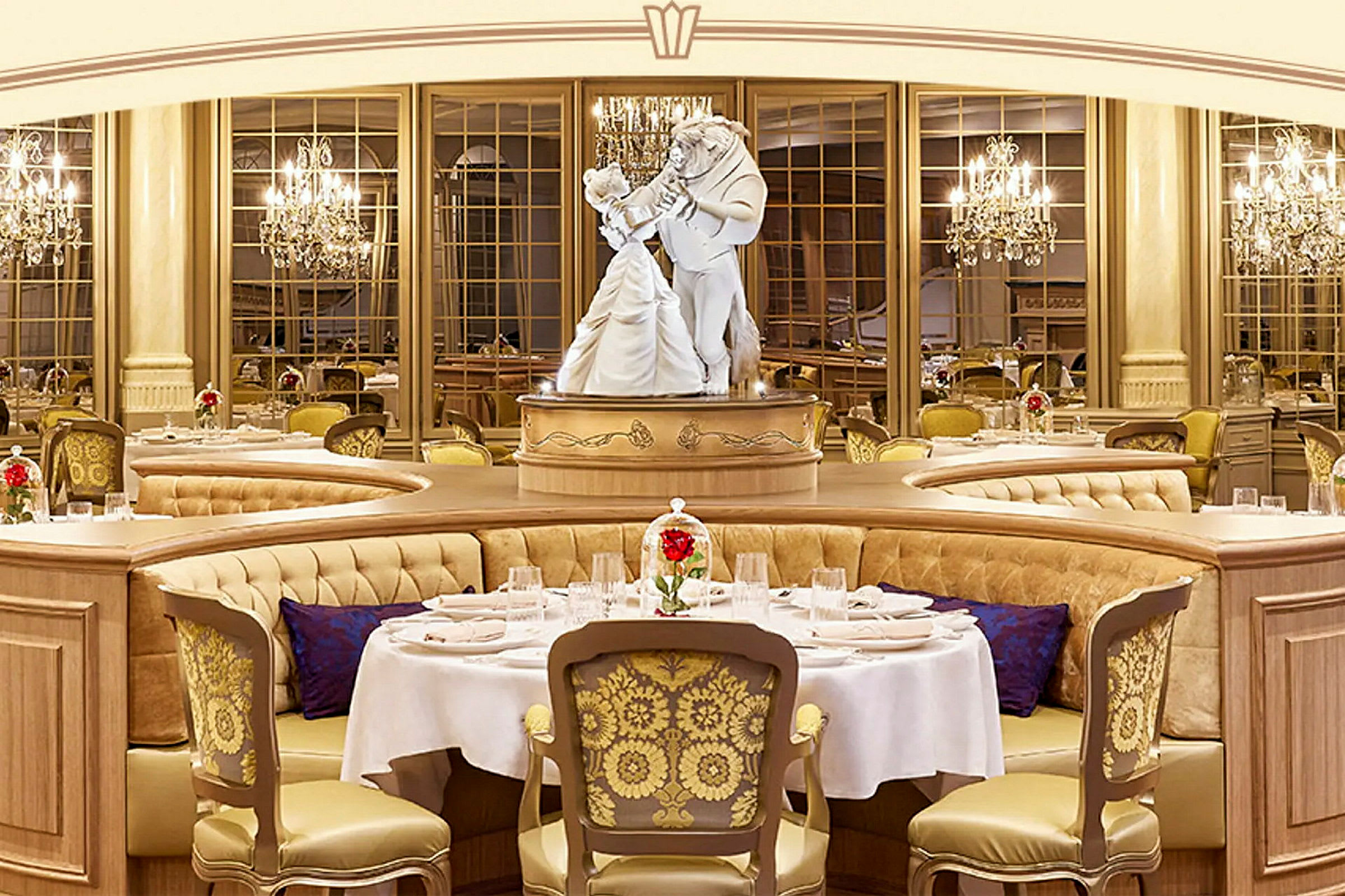 En bild på en elegant restaurang med lyxiga möbler och en staty föreställande två dansande figurer i centrum. Bord är dekorerade med vita dukar och röda blommor i glasskupor. (AI-genererad text)