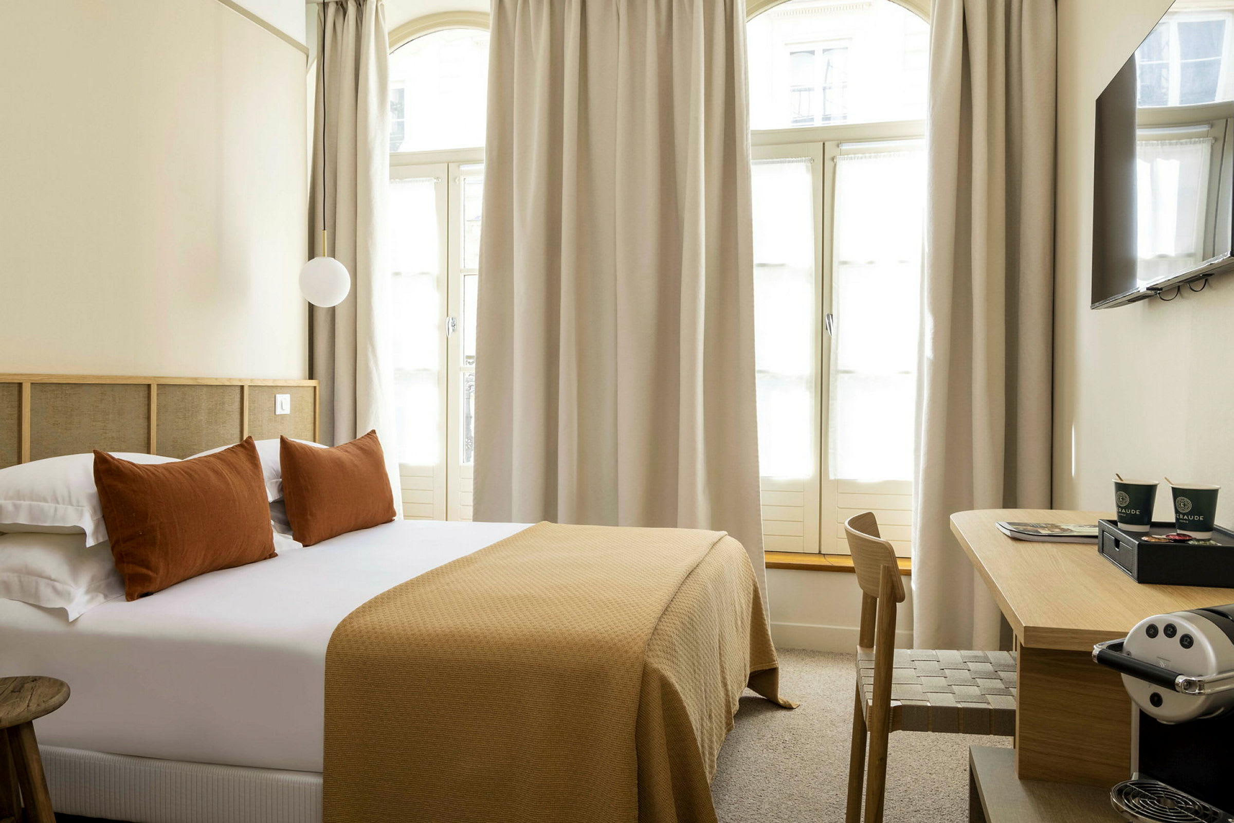 Hotellrum med en dubbelsäng, kuddar och en sängfilt i bruna toner samt ett skrivbord med en kaffemaskin. (AI-genererad text)