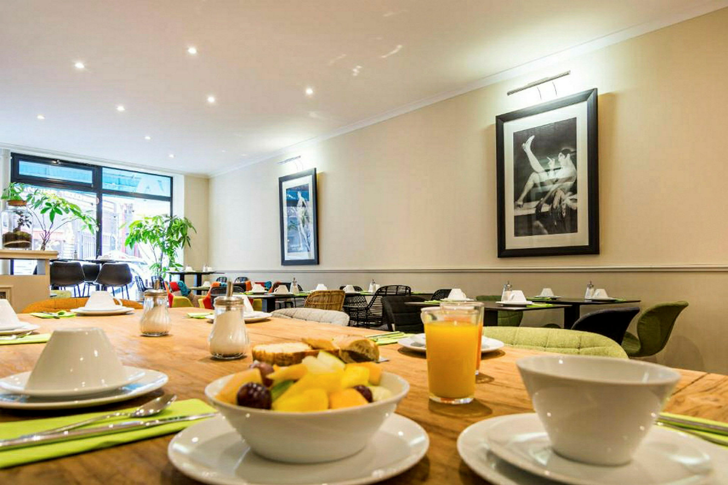 Ett dukat bord med frukost, med juice och fruktsallad samt en matsal i bakgrunden. (AI-genererad text)