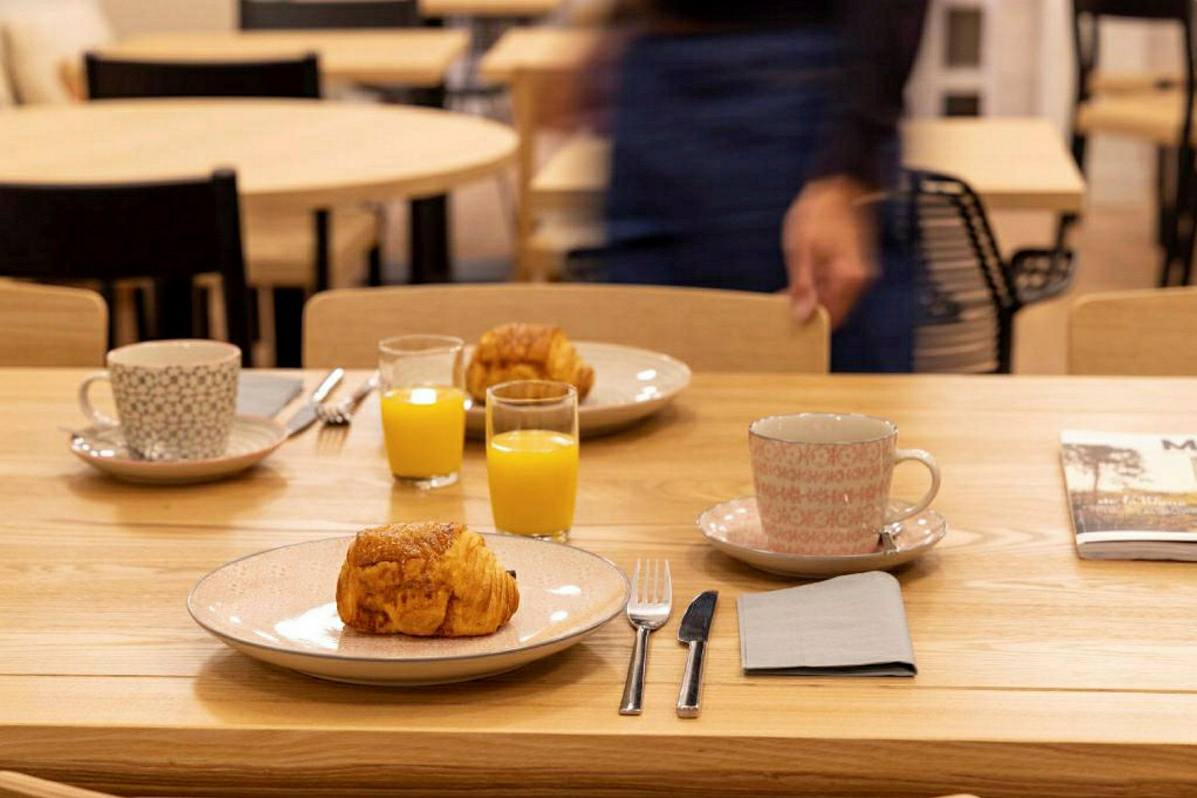 Ett bord dukat med tallrikar, croissanter, koppar och glas med apelsinjuice. (AI-genererad text)