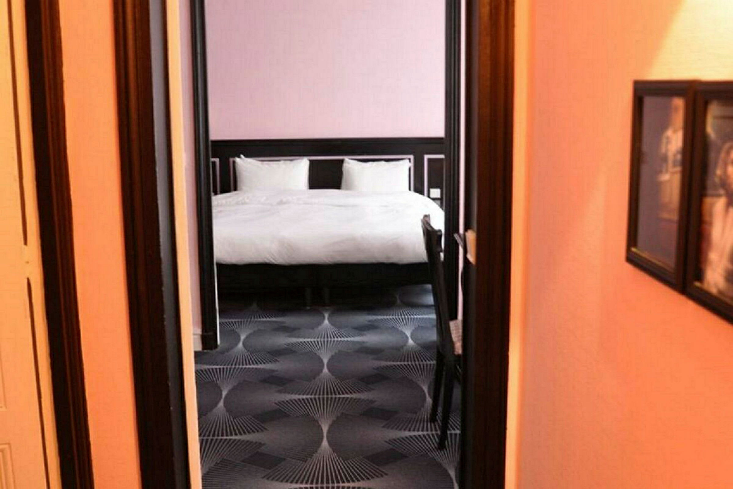 Hotellrumsinteriör med en säng sedd genom en dörröppning. (AI-genererad text)