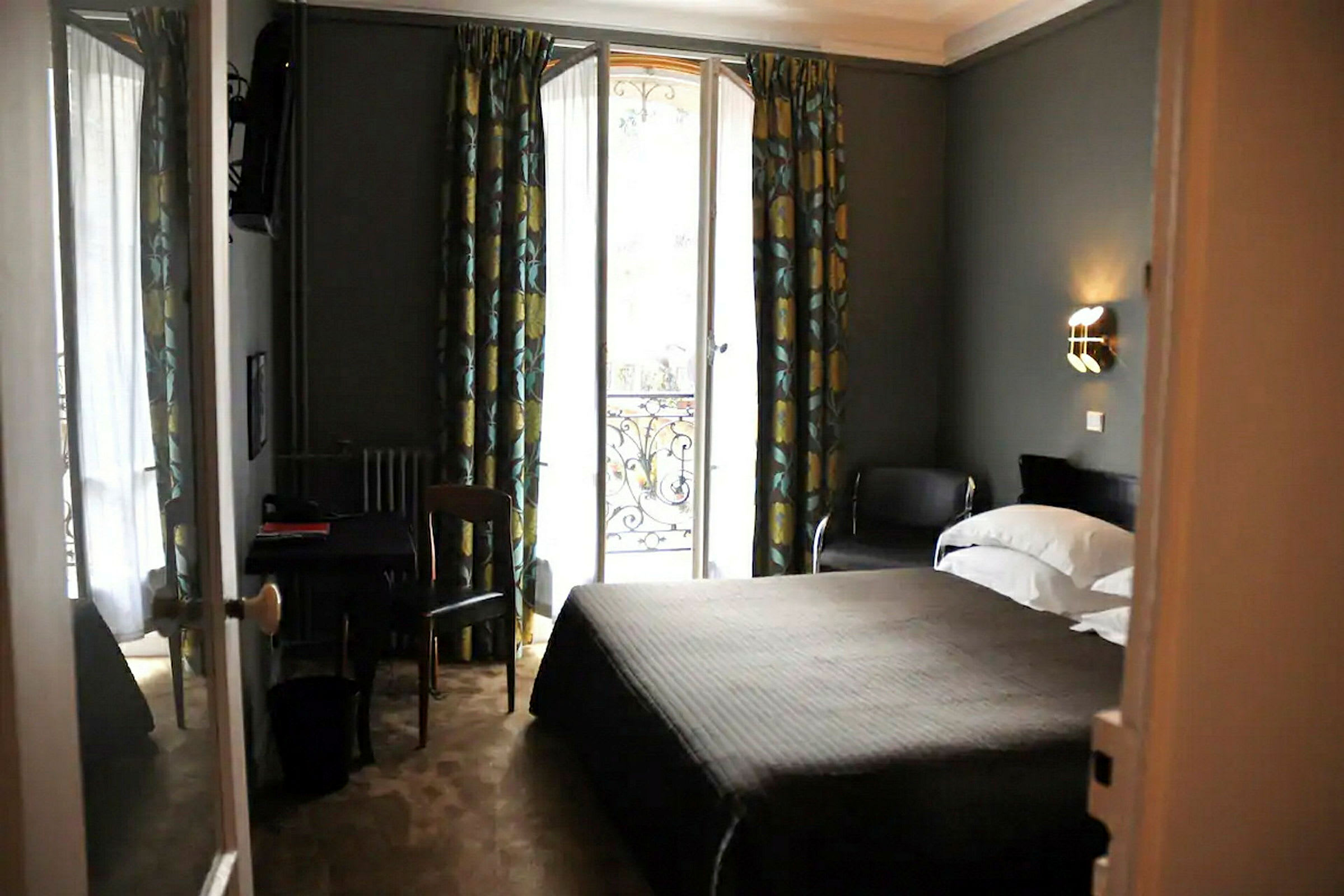 Ett hotellrum med en dubbelsäng, ett bord och en stol, samt en glasdörr med utsikt och gardiner. (AI-genererad text)