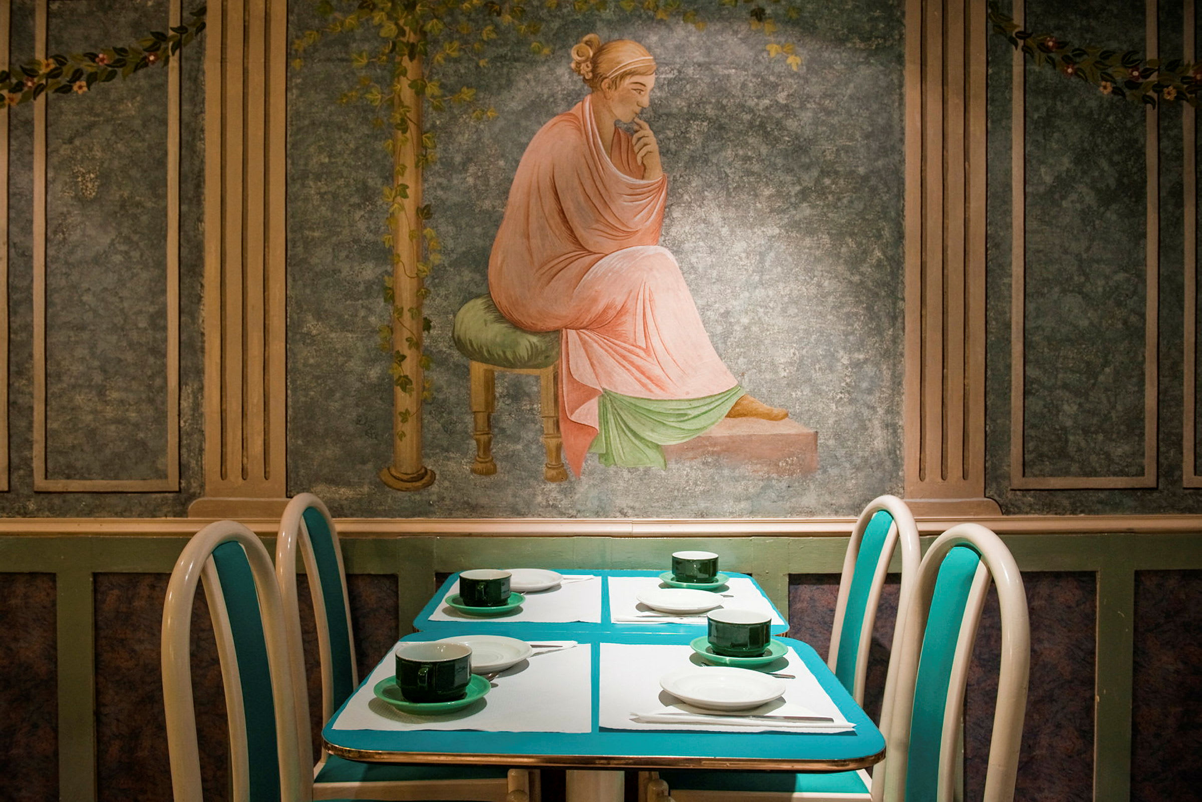 En dukad restaurangbordsuppsättning med konstnärlig väggmålning i bakgrunden. (AI-genererad text)