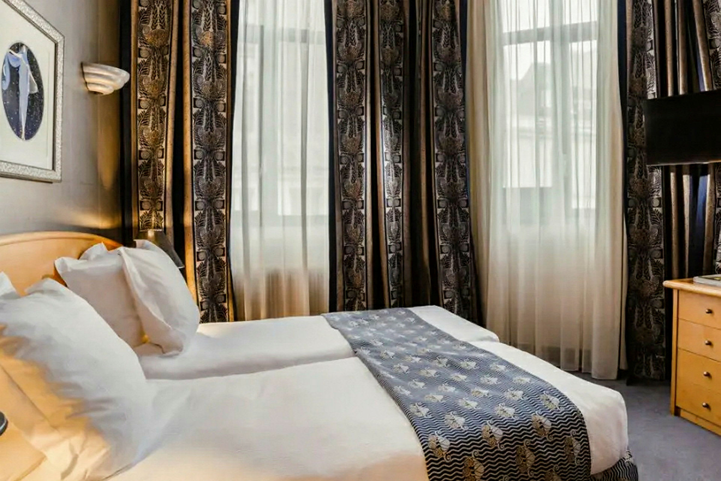 Ett hotellrum med två enkelsängar, ljusa gardiner och en dekorativ sänglöpare. (AI-genererad text)