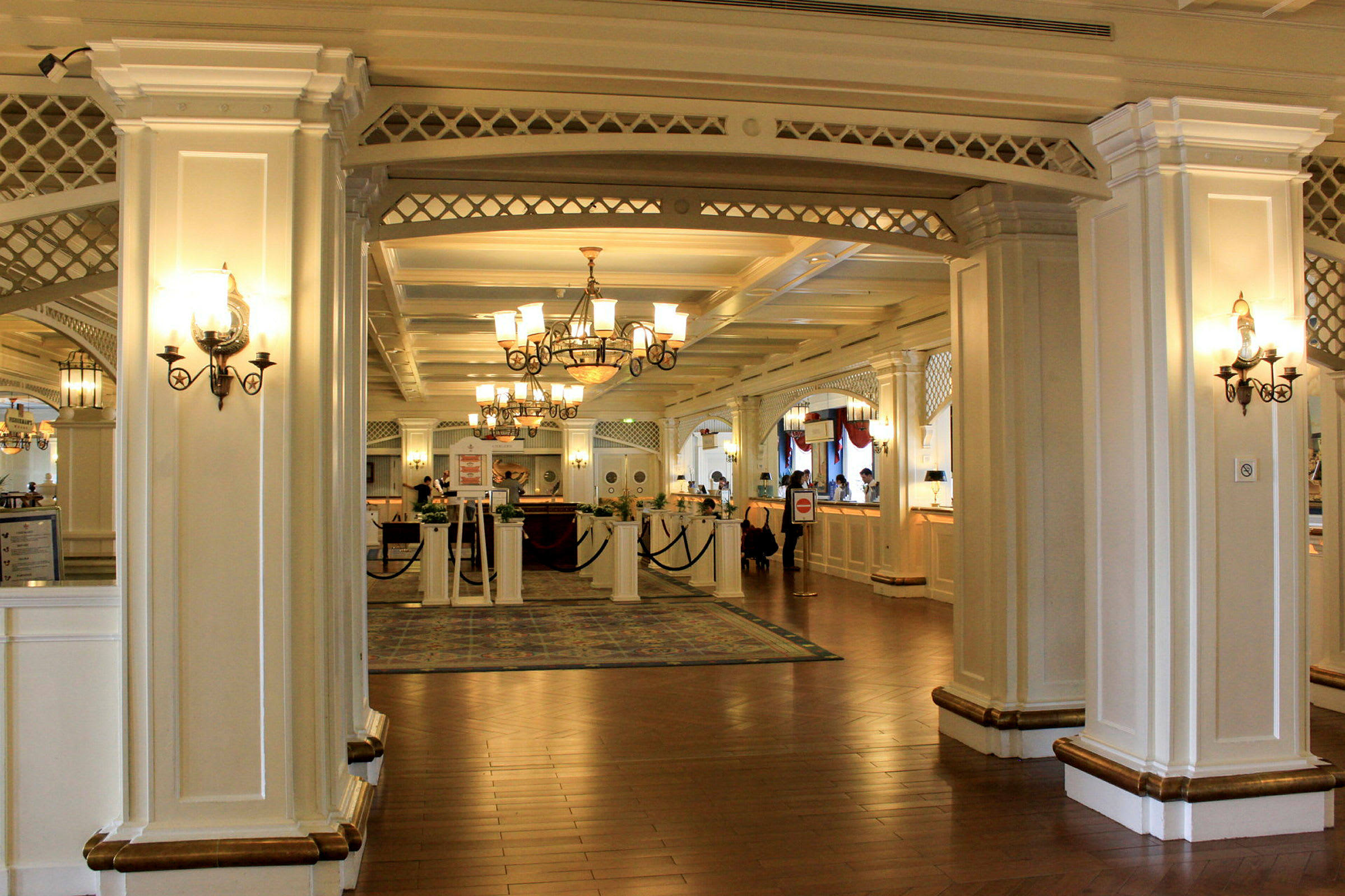 Ett elegant hotellobby med vita pelare, ljuskronor och reception. (AI-genererad text)