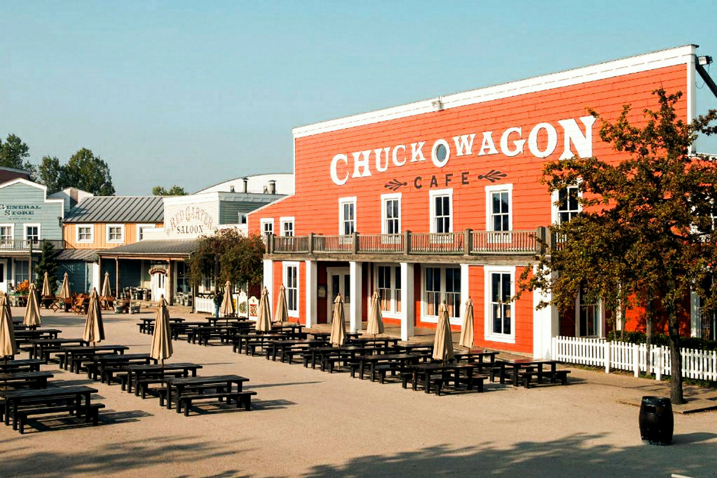 Ett område med bord och parasoller framför en byggnad med skylten 'Chuck Wagon Cafe'. (AI-genererad text)