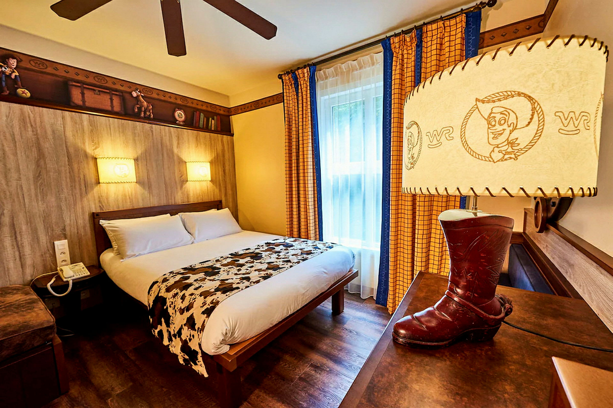 Ett tematiserat hotellrum med en dubbelsäng, dekorerat med leksaksinspirerade detaljer och en lampa formad som en cowboystövel. (AI-genererad text)