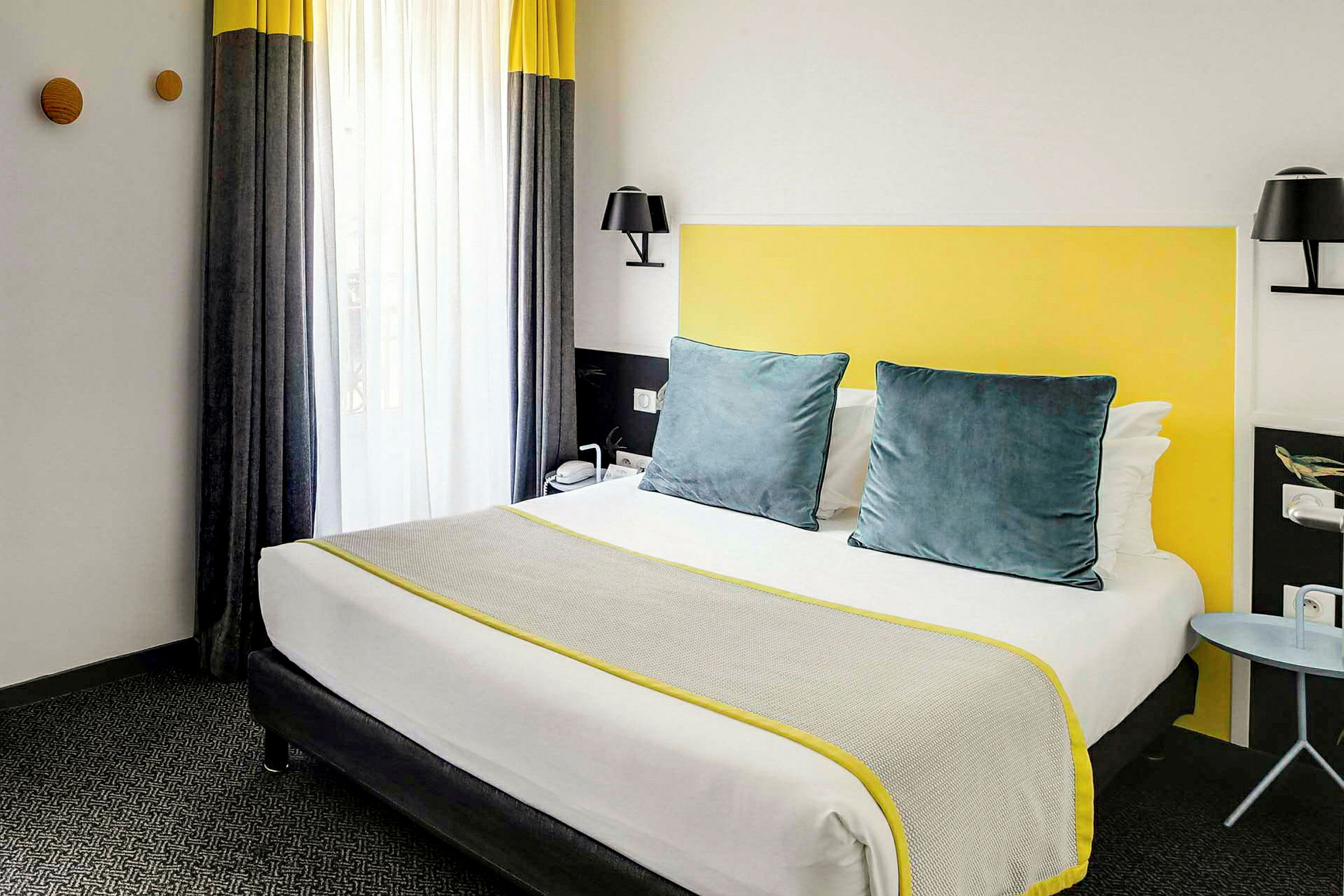 Ett hotellrum med en säng utrustad med grå och gula detaljer. (AI-genererad text)