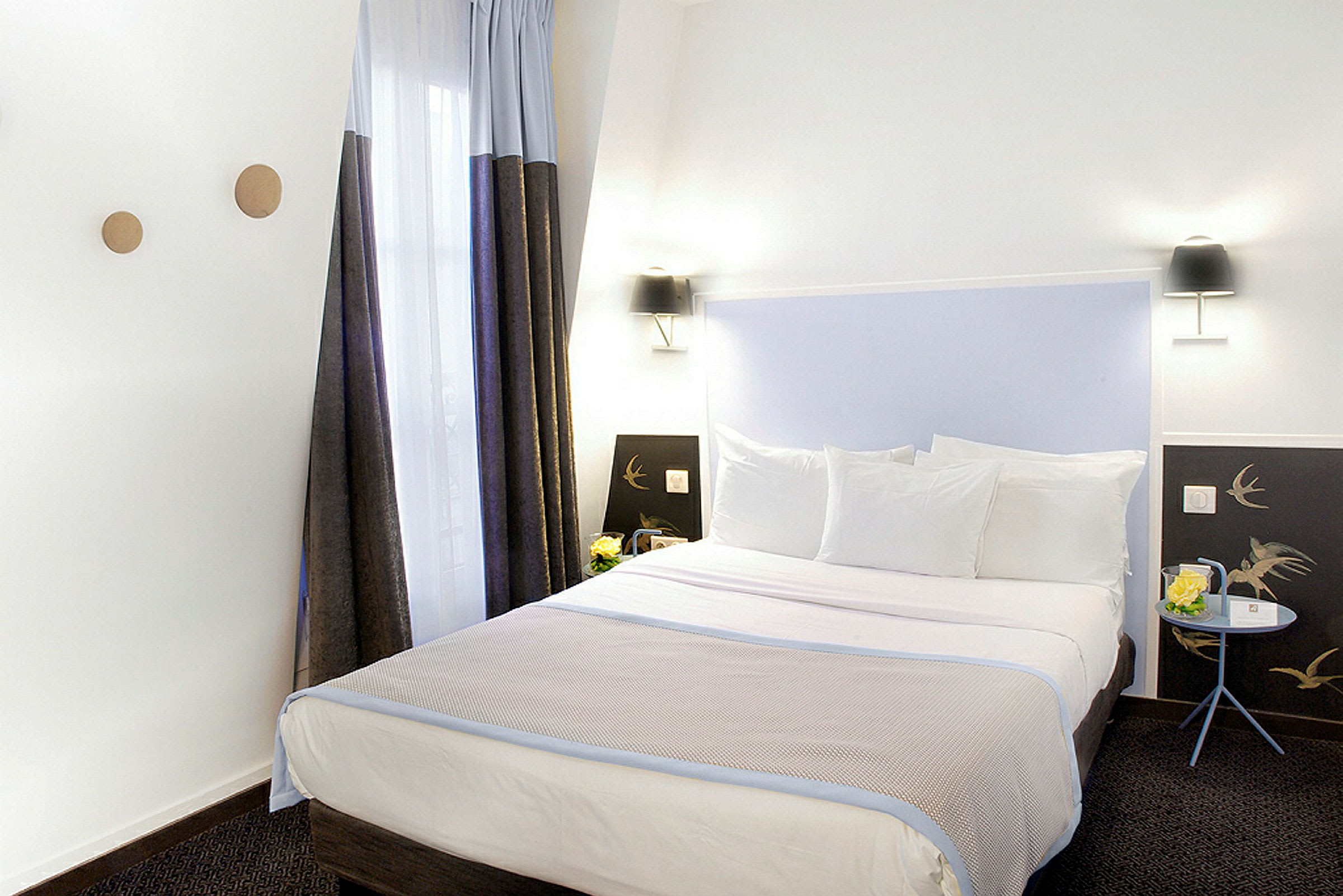 En hotellsäng med vita sängkläder är placerad i ett rum med vita väggar, gardiner och dekorativa element. (AI-genererad text)