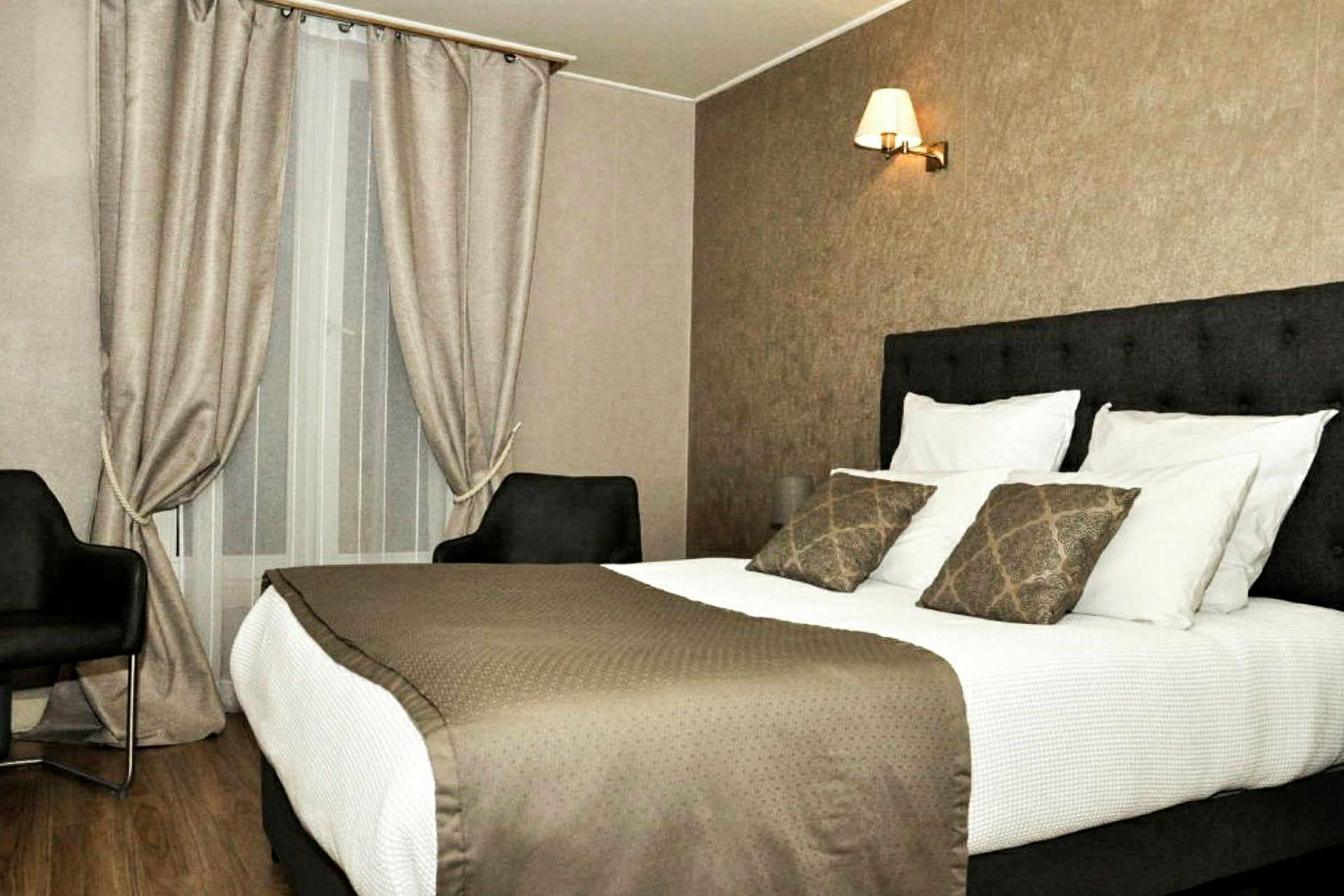 Ett hotellrum med en dubbelsäng, två fåtöljer och ett fönster med gardiner. (AI-genererad text)