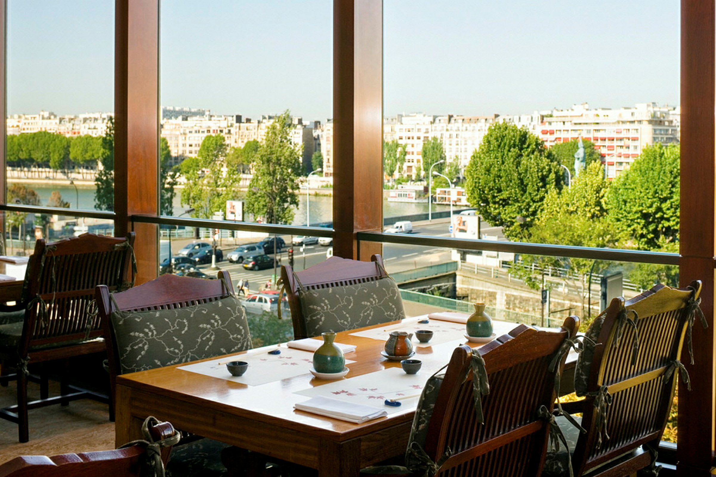 En restaurang med bord och stolar nära ett stort fönster med utsikt över staden och floden. (AI-genererad text)