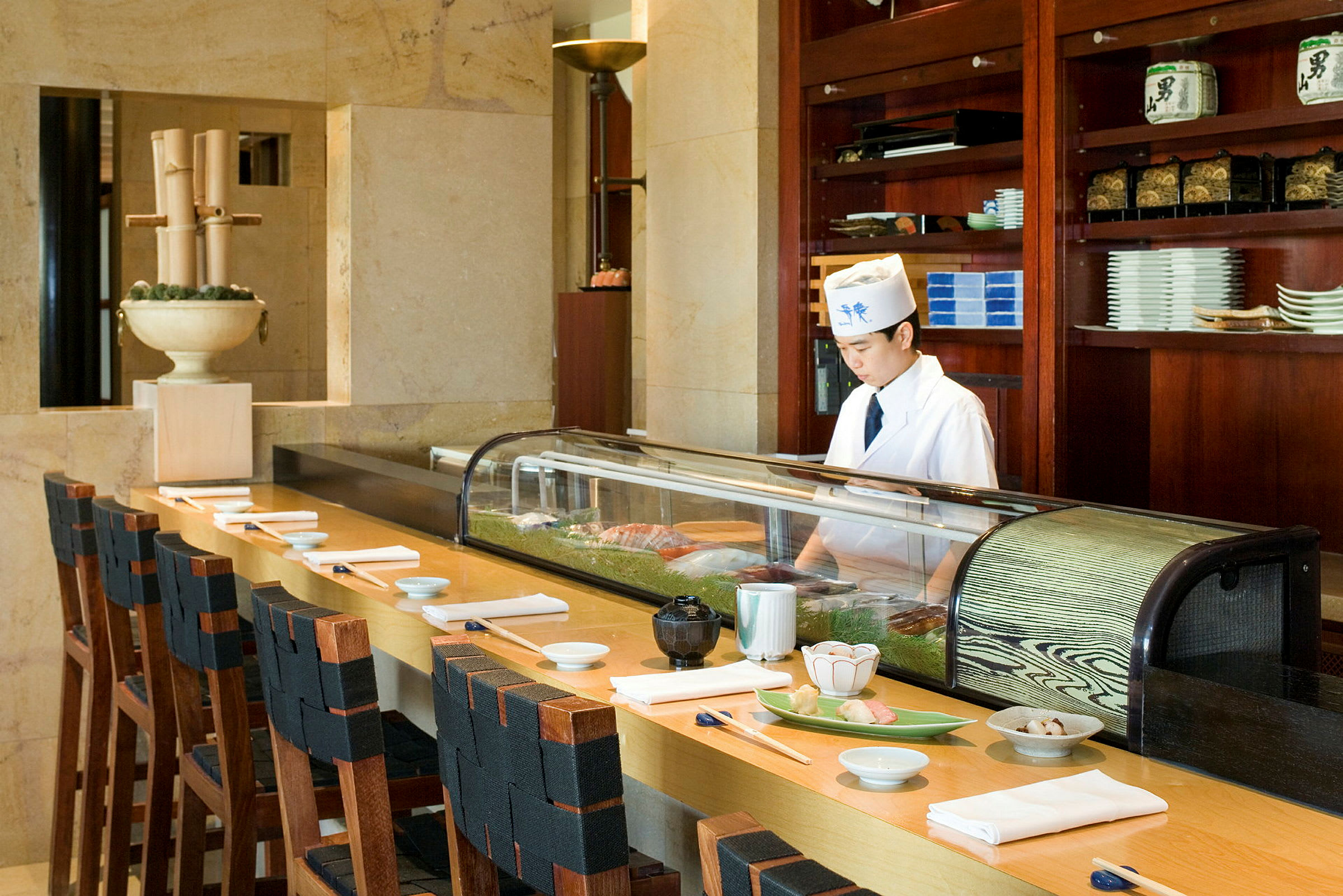 En sushi-bar med stolar vid en disk, förberedd med tallrikar och ätpinnar. (AI-genererad text)