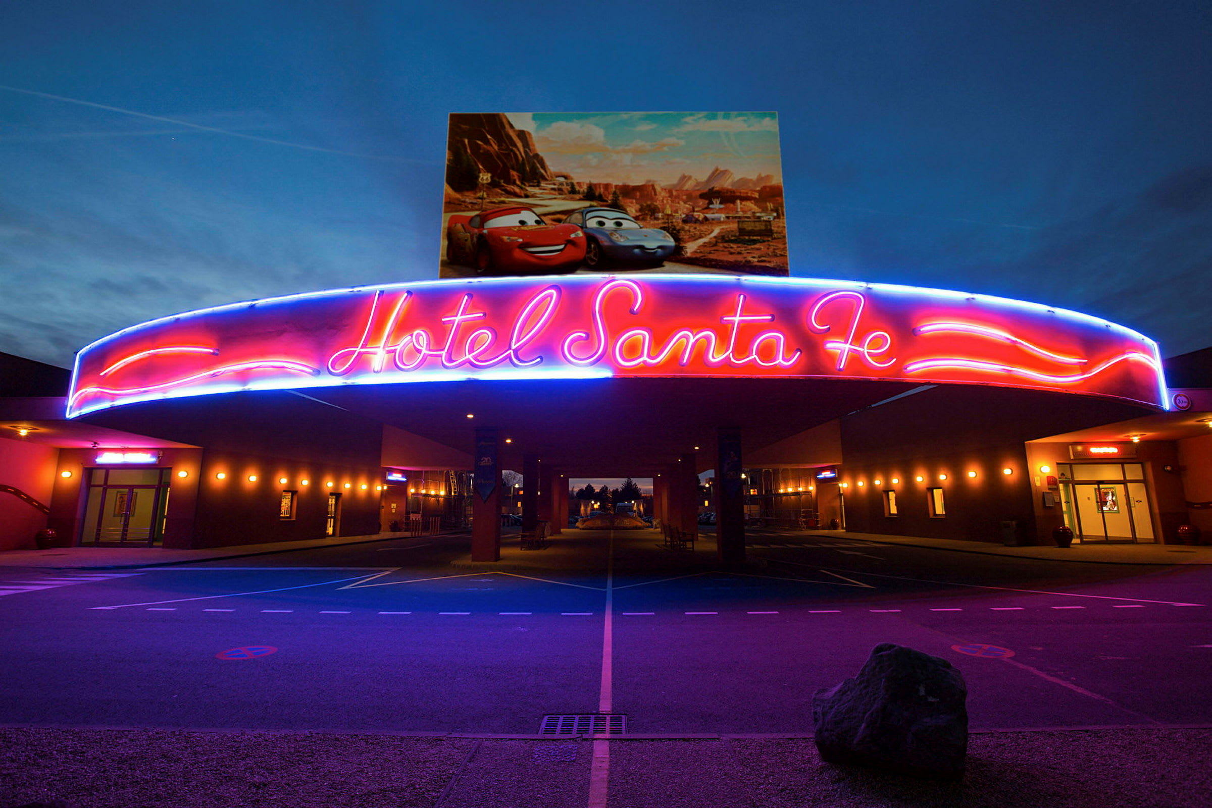 Neonskylten över entrén till Hotell Santa Fe med Disney/Pixar-bilar på affischen ovanför. (AI-genererad text)