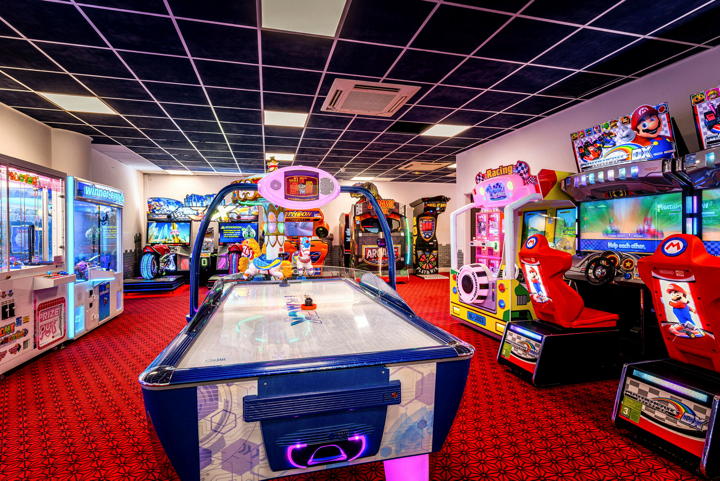 En bild på ett spelarkadrum med olika spelmaskiner och en air hockey-maskin i förgrunden. (AI-genererad text)