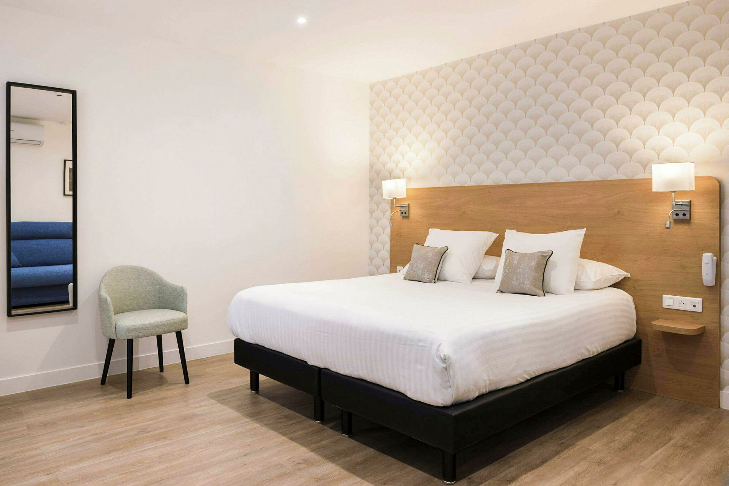 Interiör av ett hotellrum med en dubbelsäng, en grå stol och en spegel på väggen. (AI-genererad text)