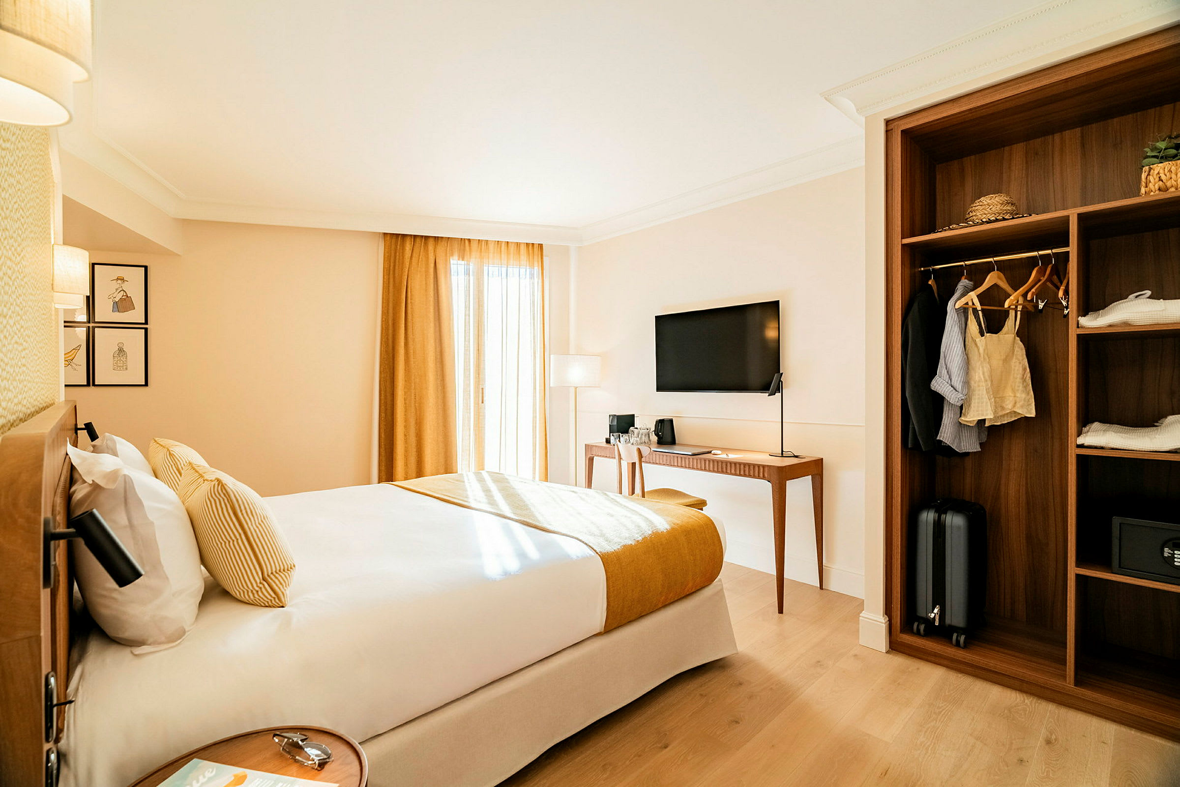 Ett hotellrum med en dubbelsäng, en TV på väggen, ett skrivbord och en garderob med kläder och bagage. (AI-genererad text)