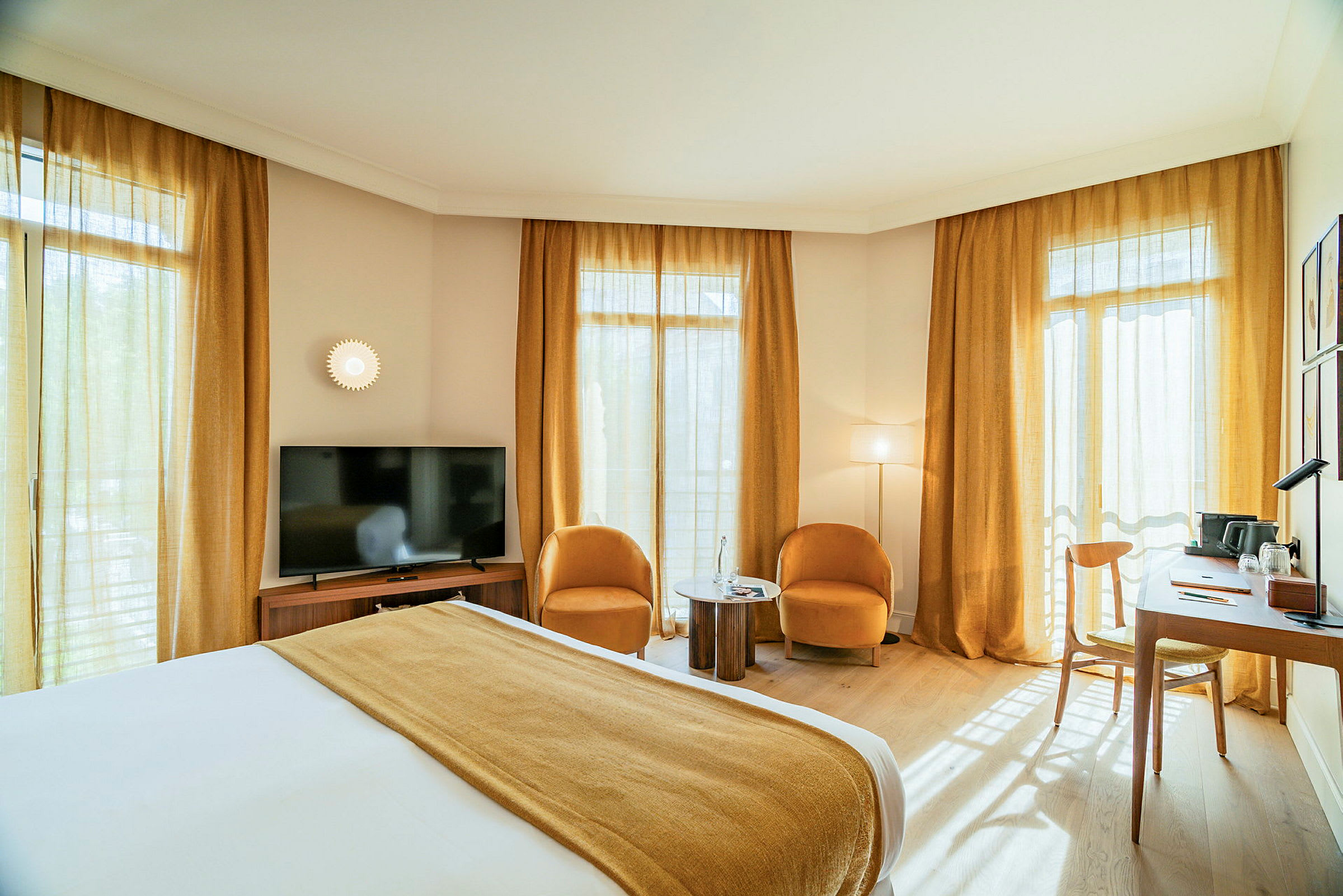 Ett hotellrum med en dubbelsäng, två fåtöljer och ett litet bord, en TV och ett skrivbord vid fönstren. (AI-genererad text)