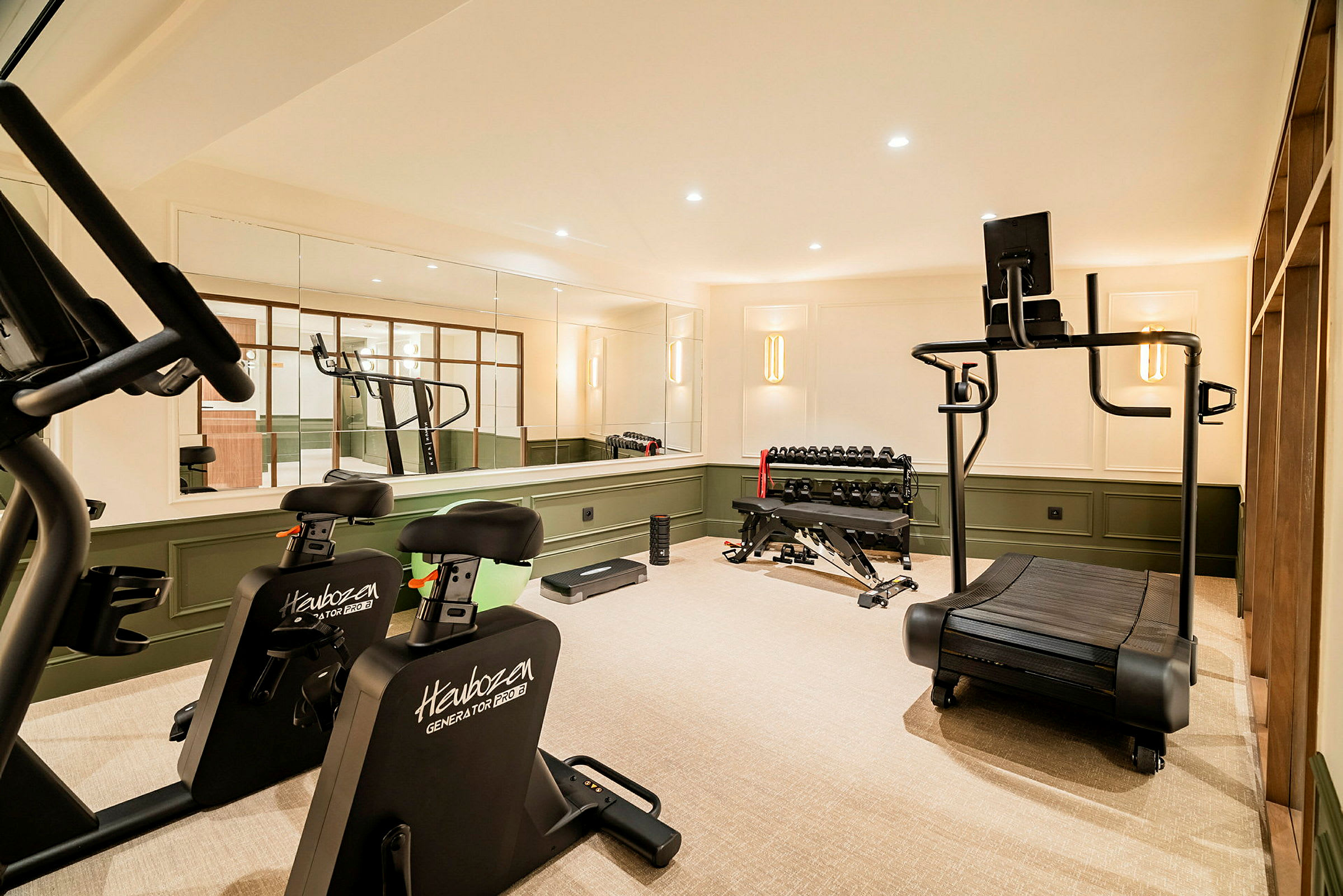 Ett gym med träningsutrustning som löpband, träningscyklar, hantlar och träningsbänk. (AI-genererad text)