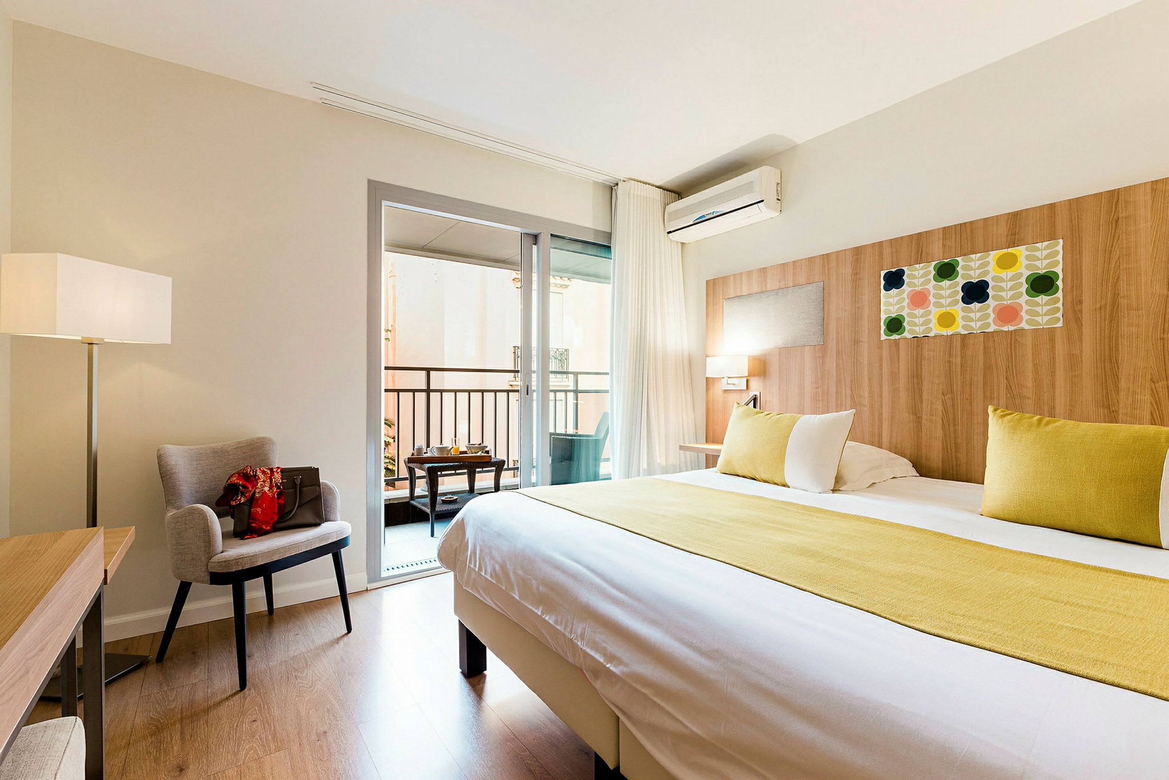Ett hotellrum med en stor säng, en fåtölj, ett skrivbord, och en balkong. (AI-genererad text)