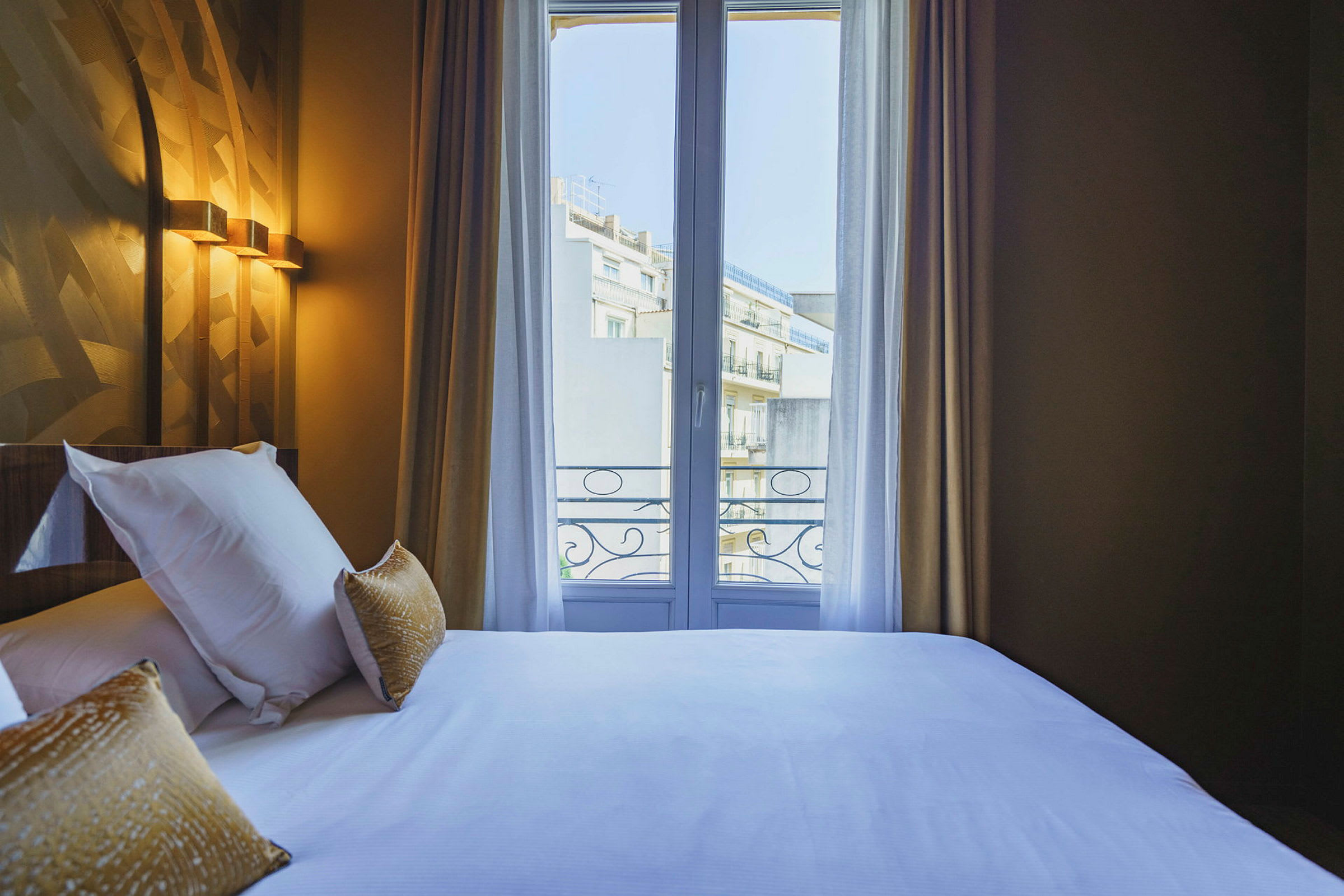 Ett hotellrum med en säng nära ett fönster med utsikt över en byggnad. (AI-genererad text)