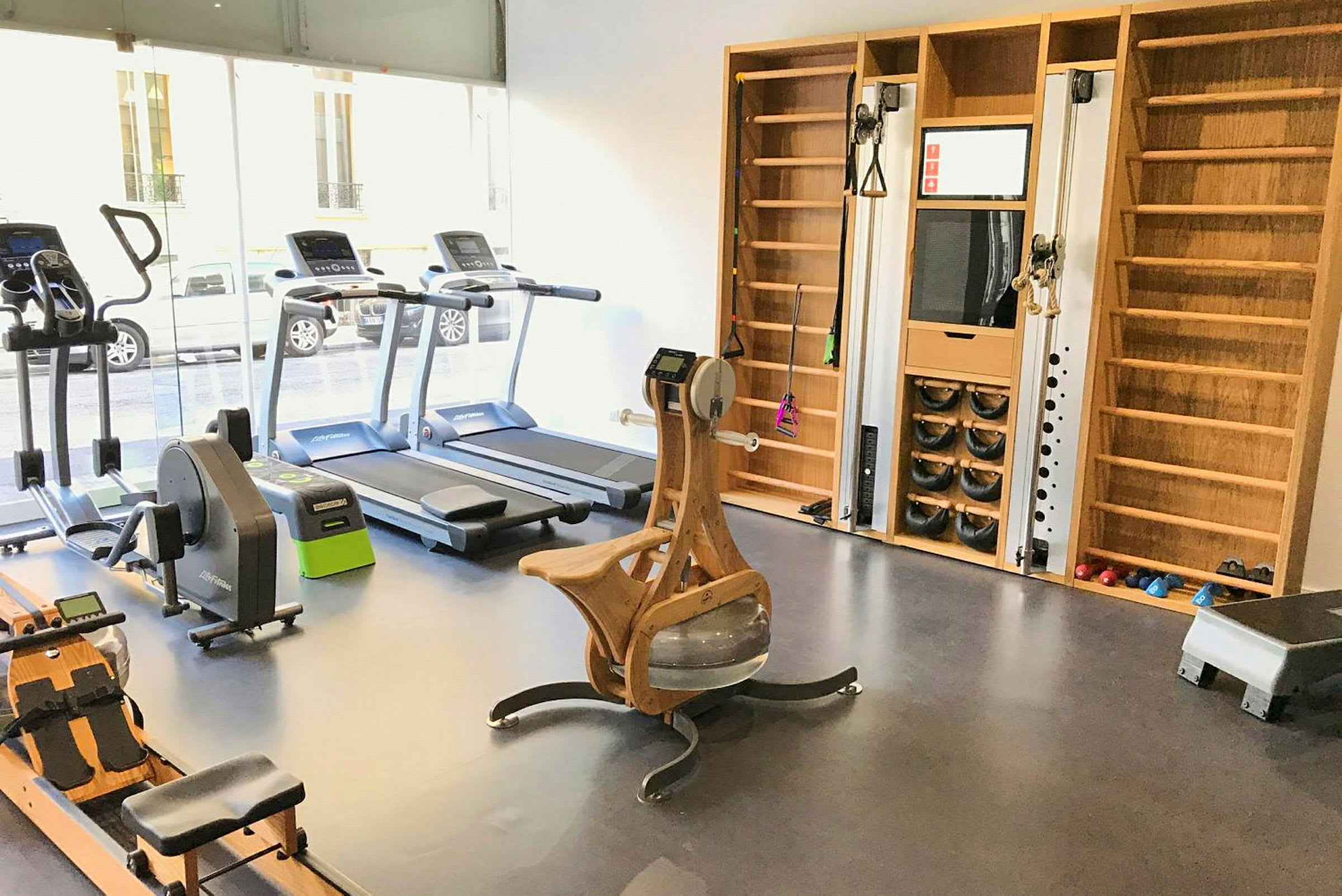 Ett välutrustat gym med träningsutrustning och fönster mot gatan. (AI-genererad text)