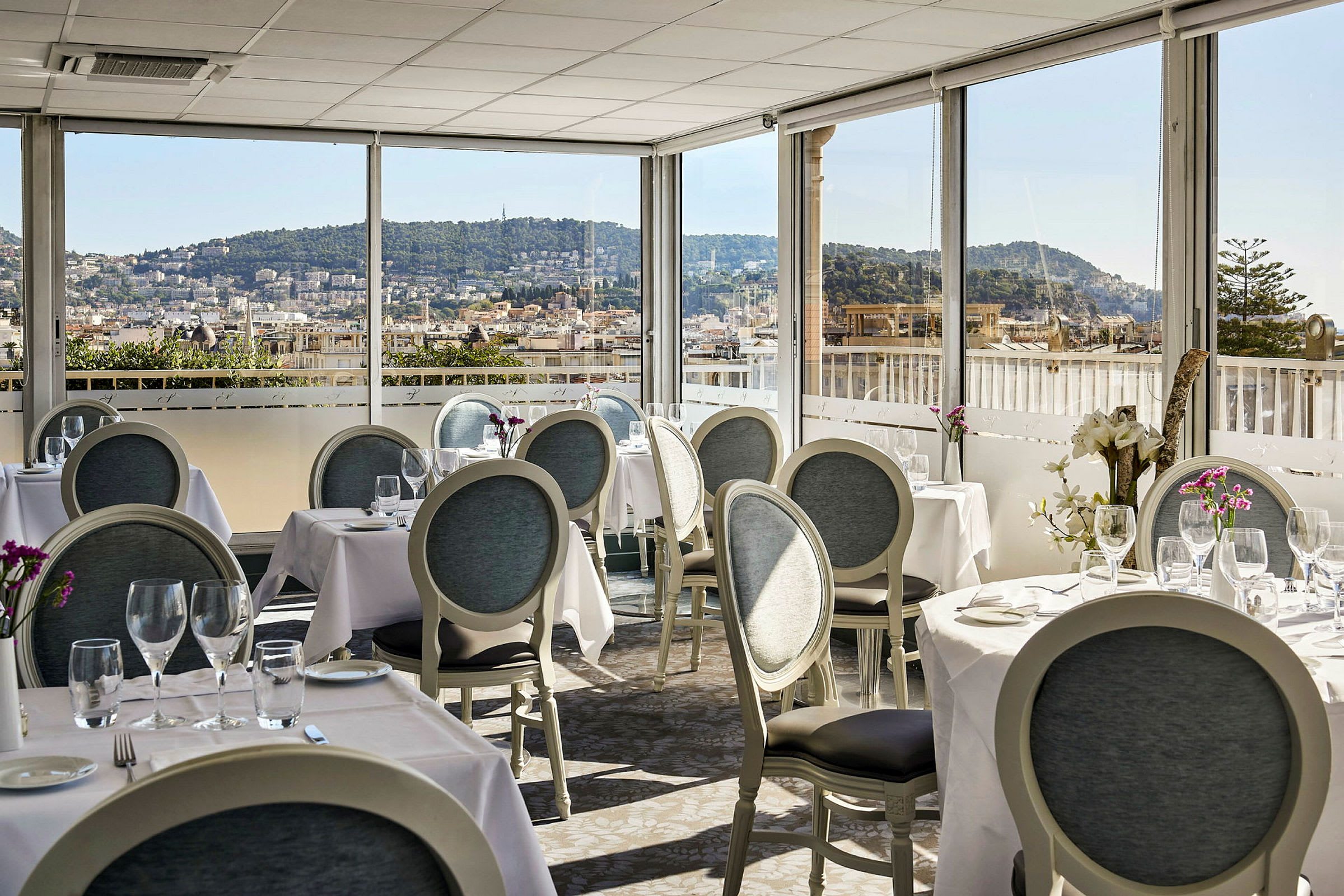 Restaurang med dukade bord och utsikt över en stad med kullar i bakgrunden. (AI-genererad text)