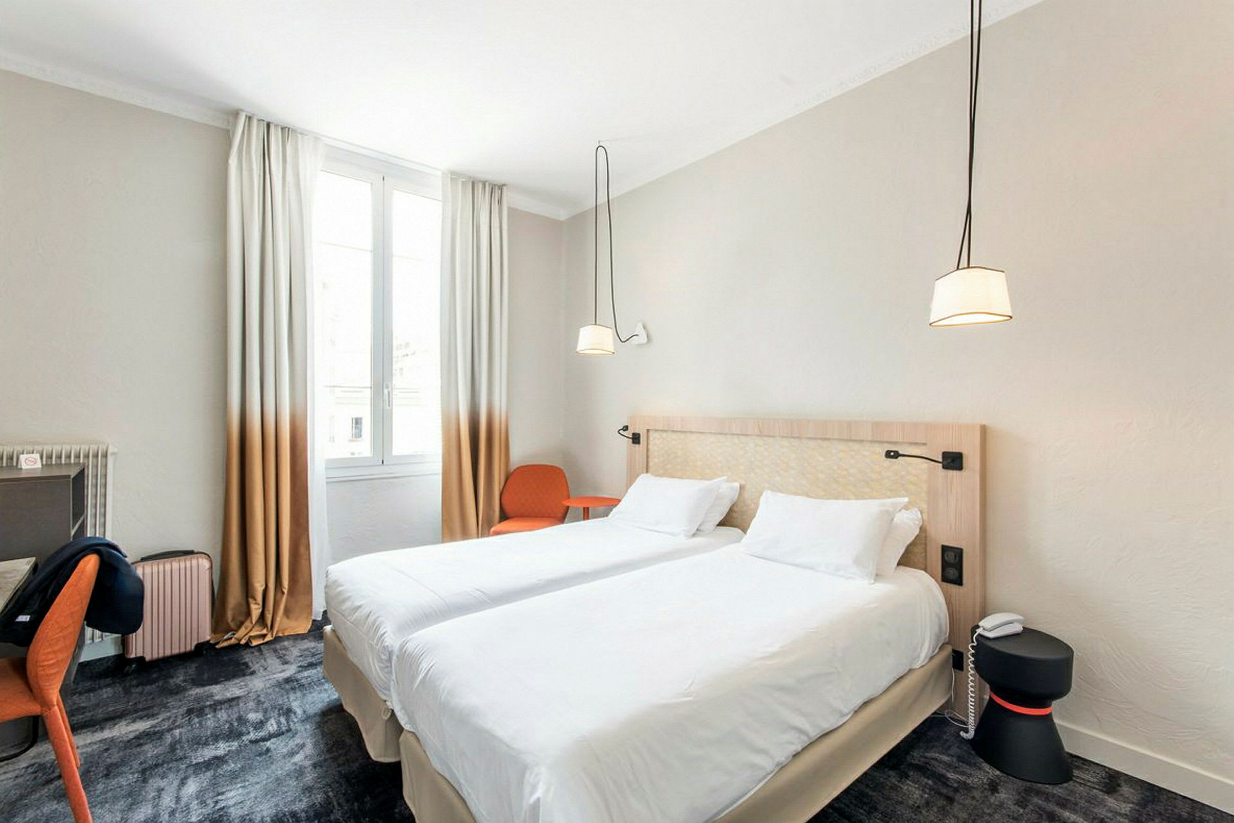 Ett hotellrum med två enförbundna enkelsängar, ett skrivbord, en stol och fönster med ljusinsläpp. (AI-genererad text)