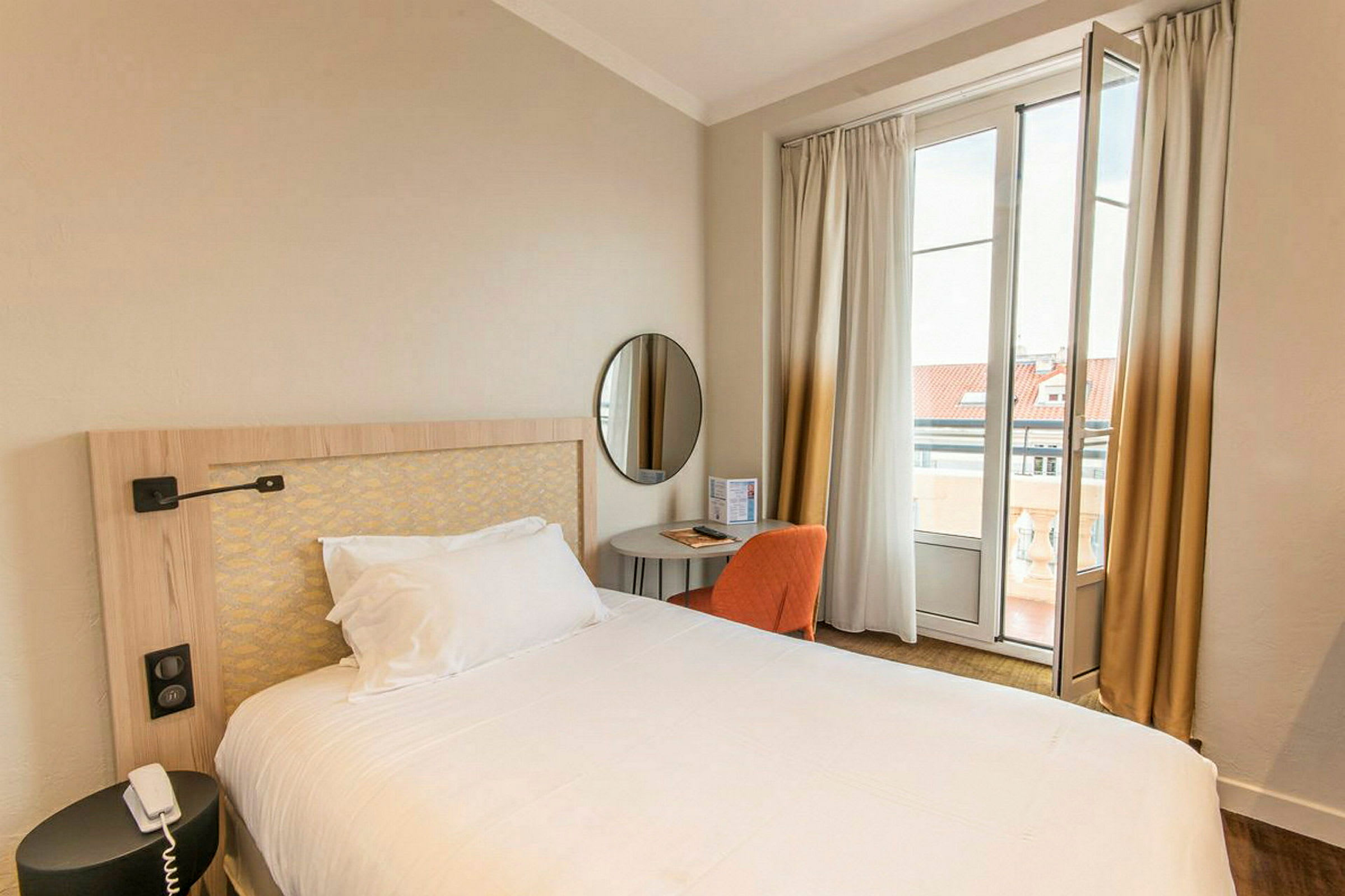 Ett hotellrum med en bäddad säng, ett litet bord och en stol framför ett fönster med gardiner. (AI-genererad text)